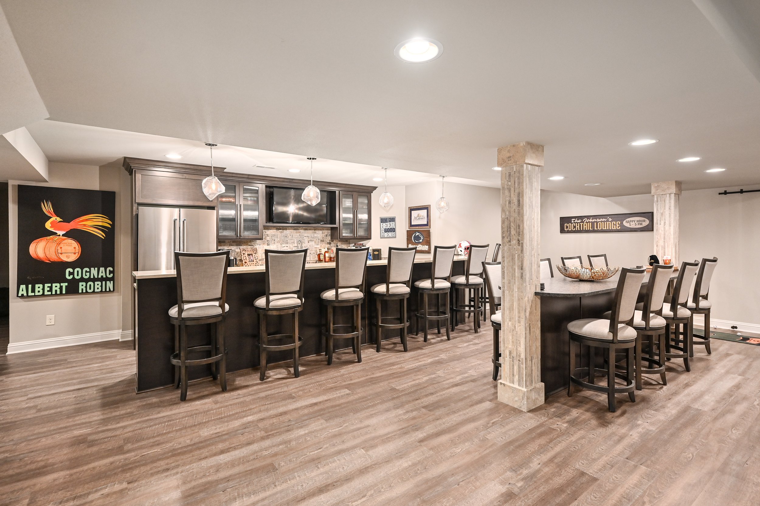 Empty bar area with high chairs, pendant lights, refrigerator, and artwork on the walls.