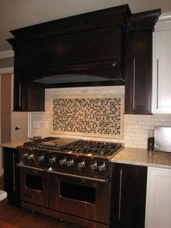 Kitchen with black cabinets, a mosaic tile backsplash behind a stainless steel stove, and beige countertop.