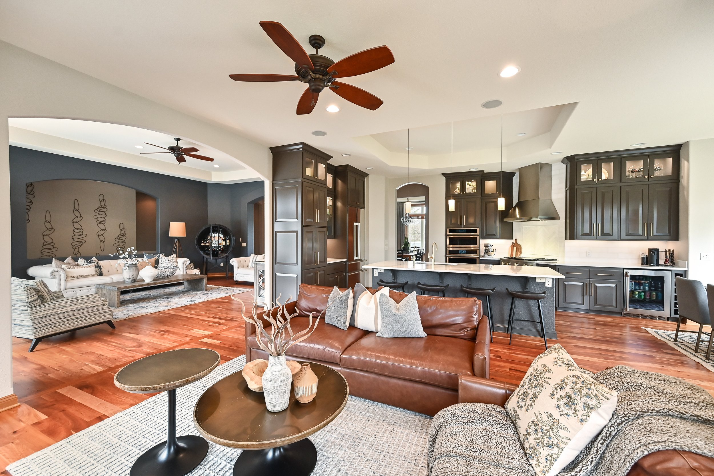 Open-concept living room and kitchen with hardwood floors, dark kitchen cabinets, white countertops, and modern furniture.
