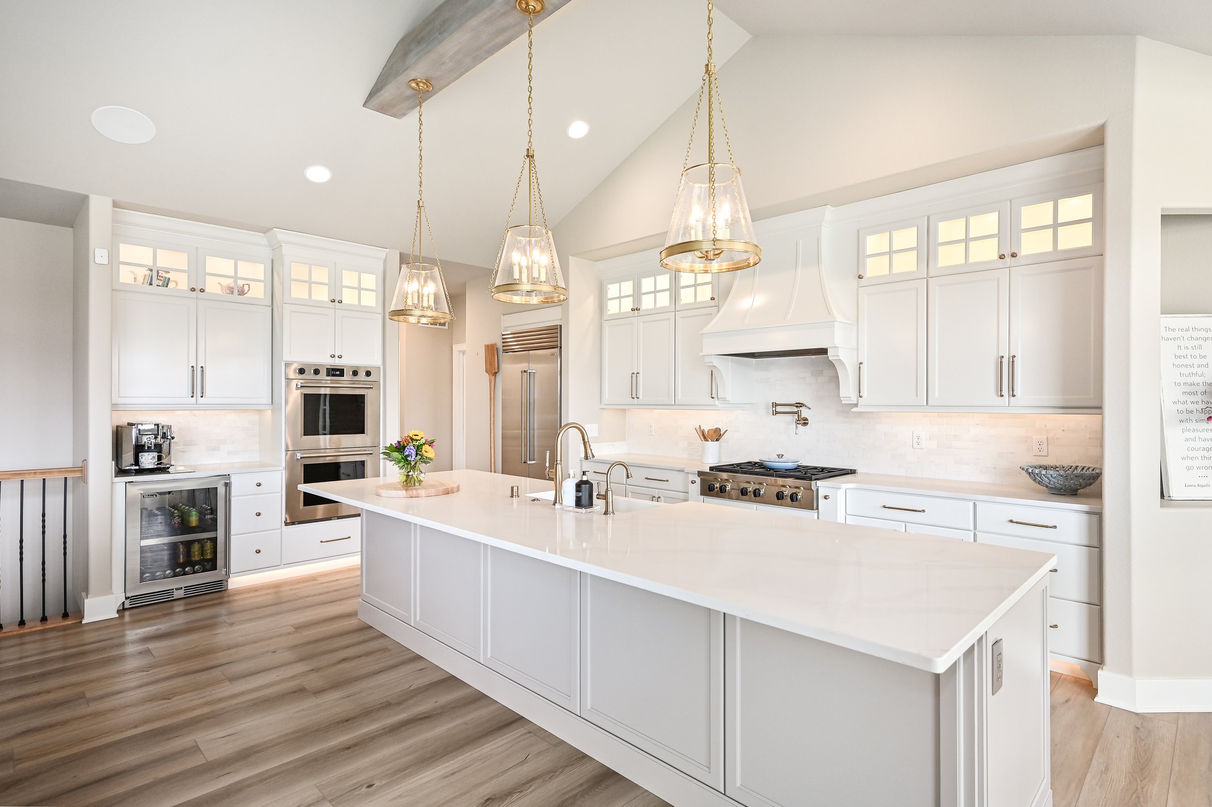 Bright white kitchen with an island, modern appliances, pendant lights, and wooden flooring.