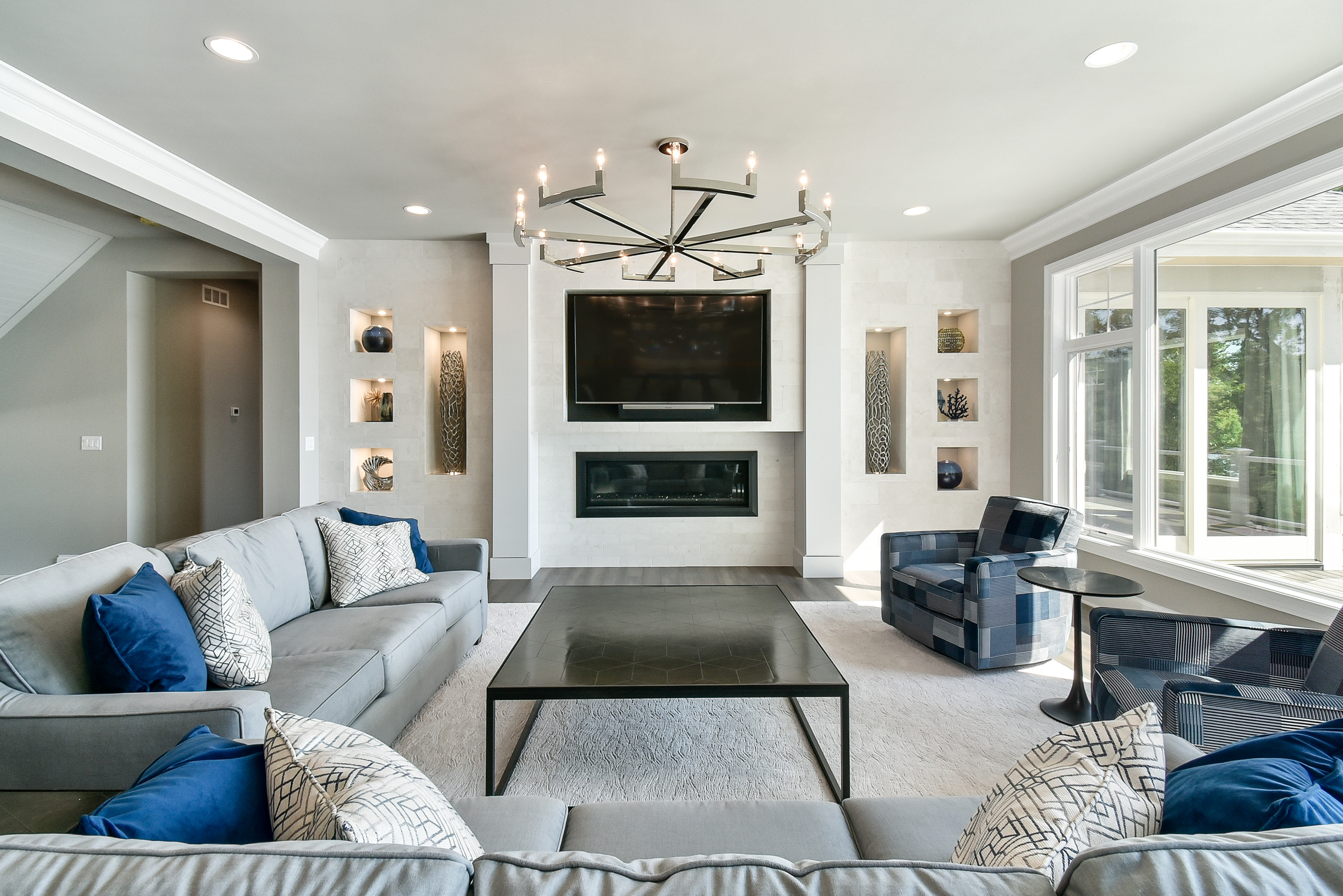 Living room with gray sofa, armchair, fireplace, television, built-in shelves, large window, and minimalist decor.