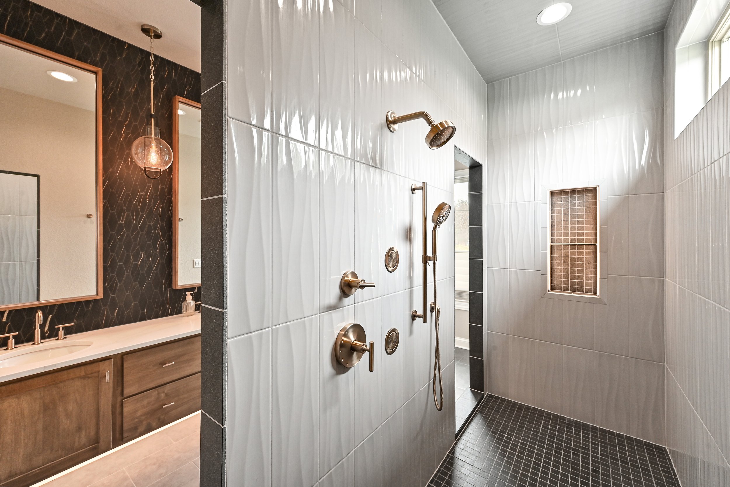Modern shower room with multiple shower heads and controls, tiled walls and floor, small window, and natural lighting.