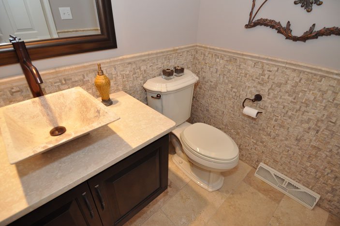 Bathroom with a stone sink, wooden vanity, toilet, mirror, and decorative wall art.