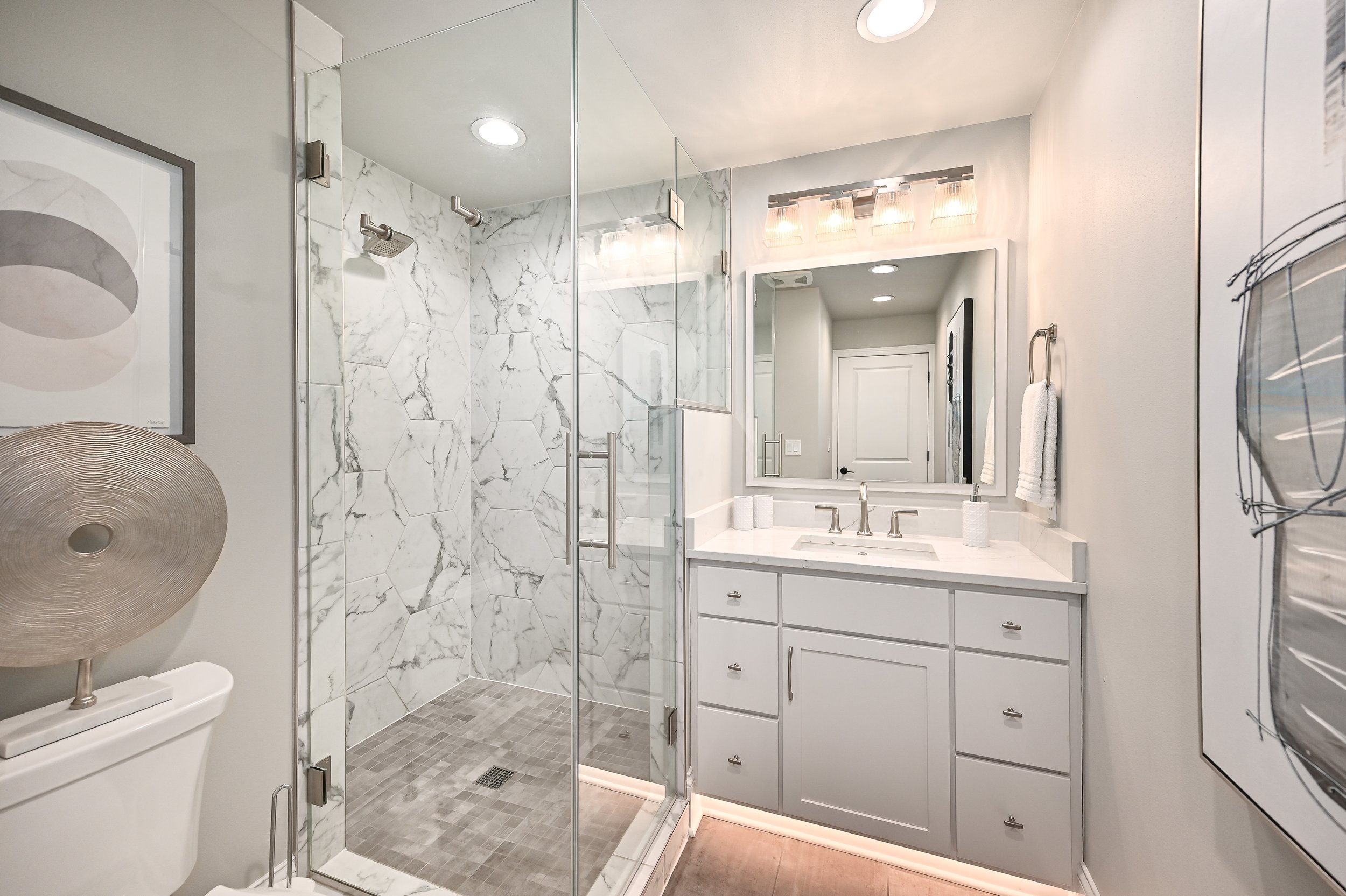 Modern bathroom with marble tile shower, white vanity with mirror, and decorative artwork.