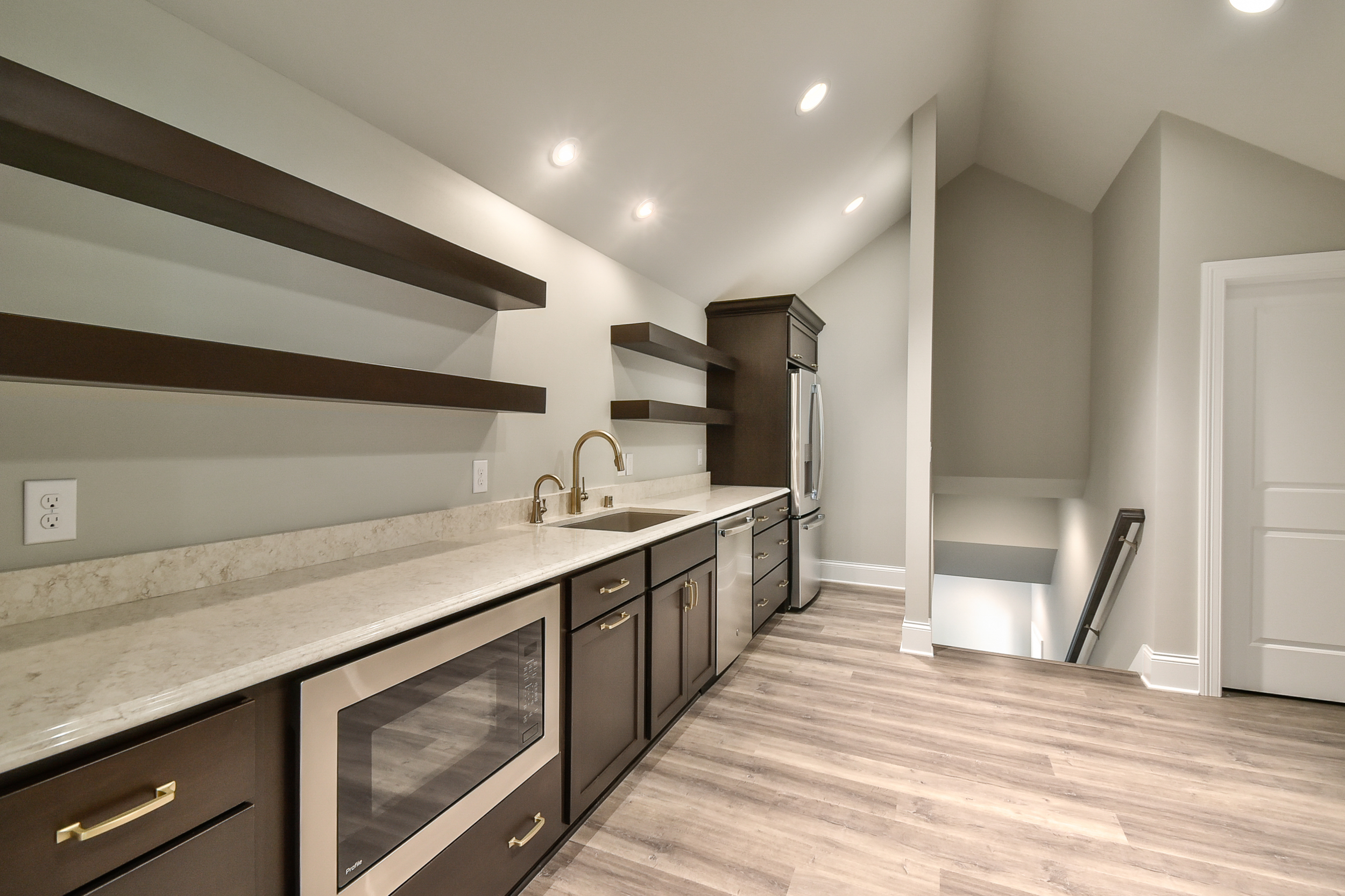 Modern kitchen with dark cabinets, beige countertops, open dark shelves, stainless steel appliances, and light wood flooring.