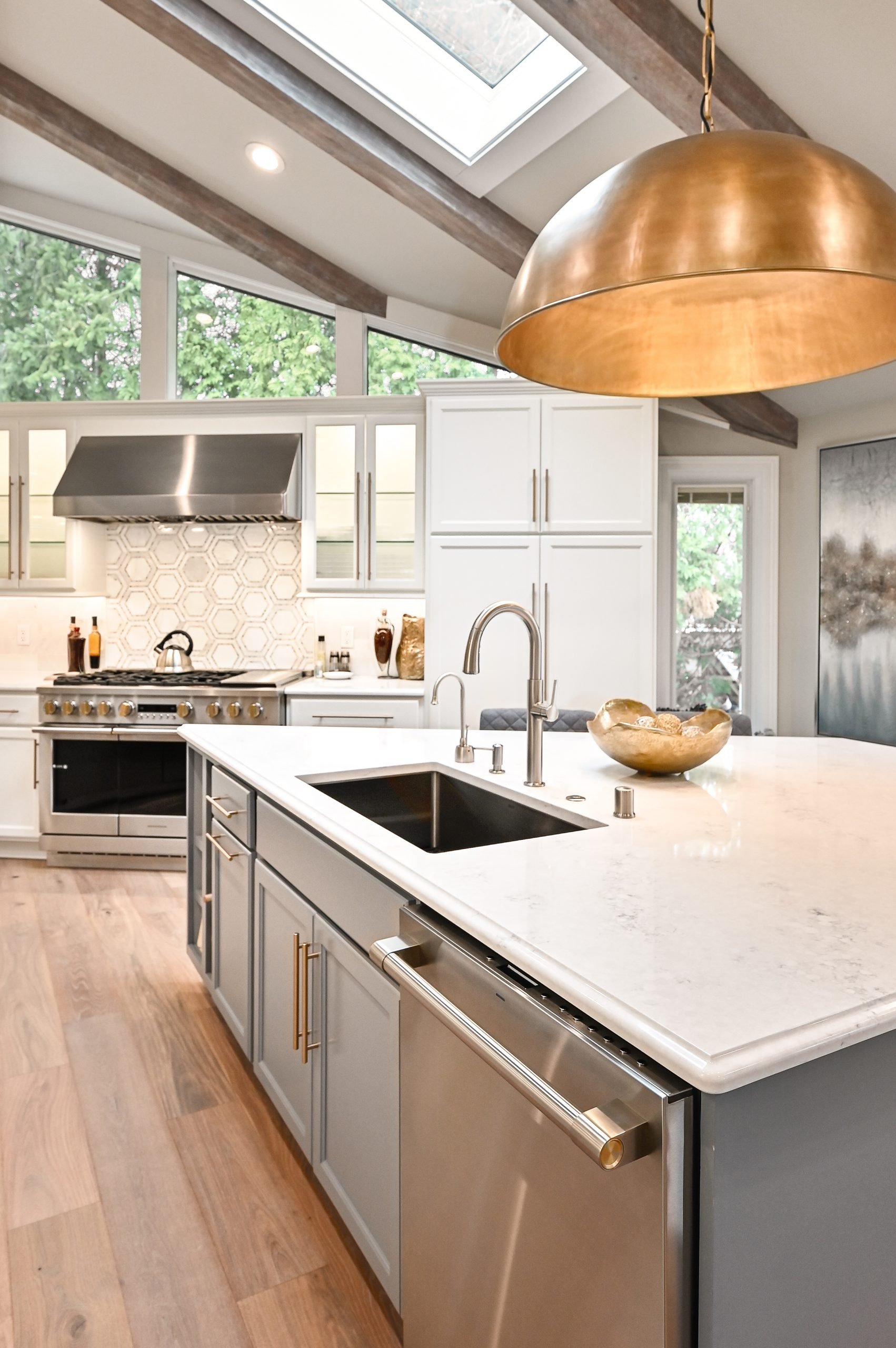 Modern kitchen with white cabinets, a large marble island, a stainless steel range with a hood, a black sink, and a large copper pendant light hanging from the ceiling.