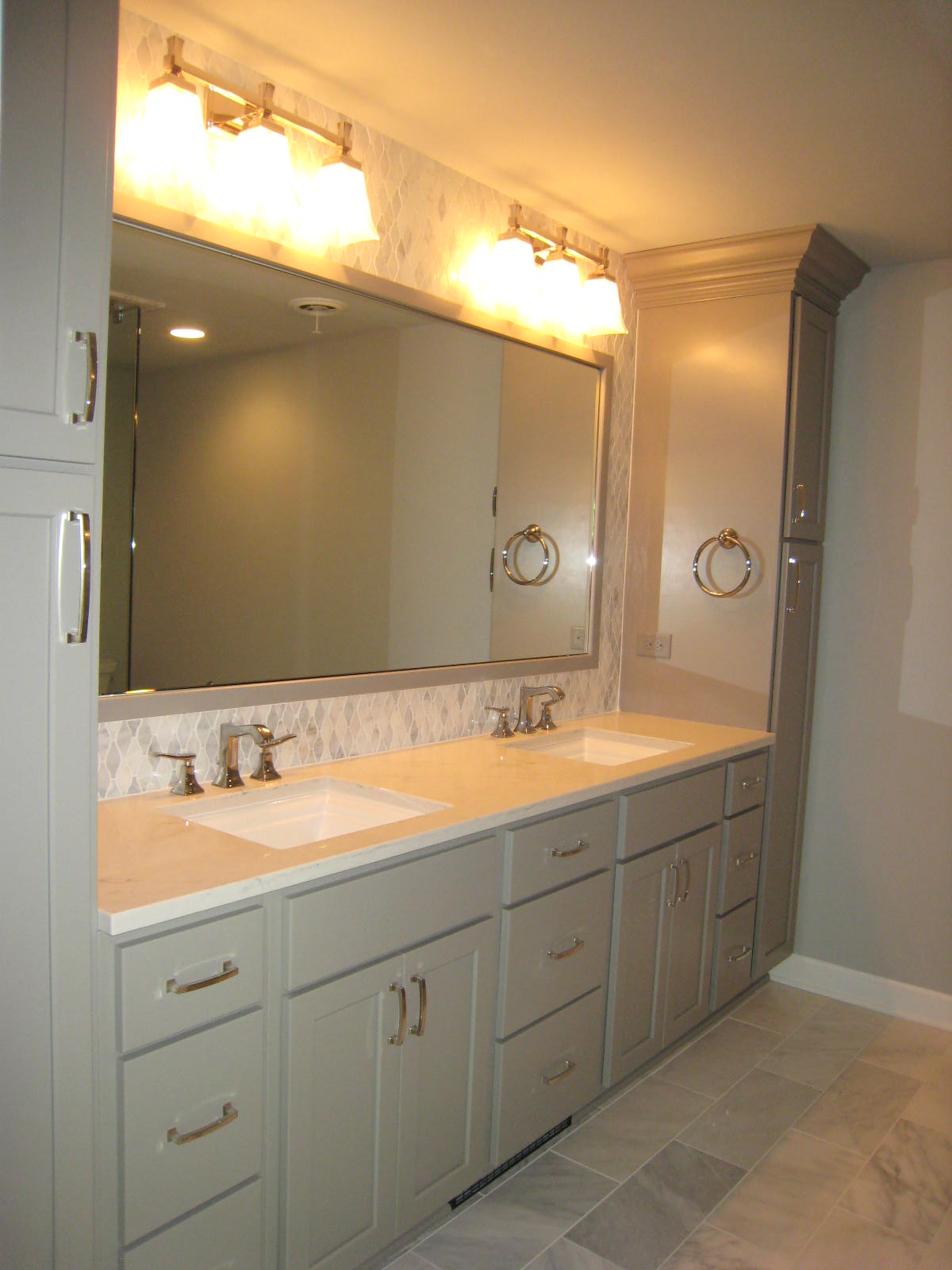 Bathroom vanity with double sinks, large mirror, overhead lighting, and light green cabinets.