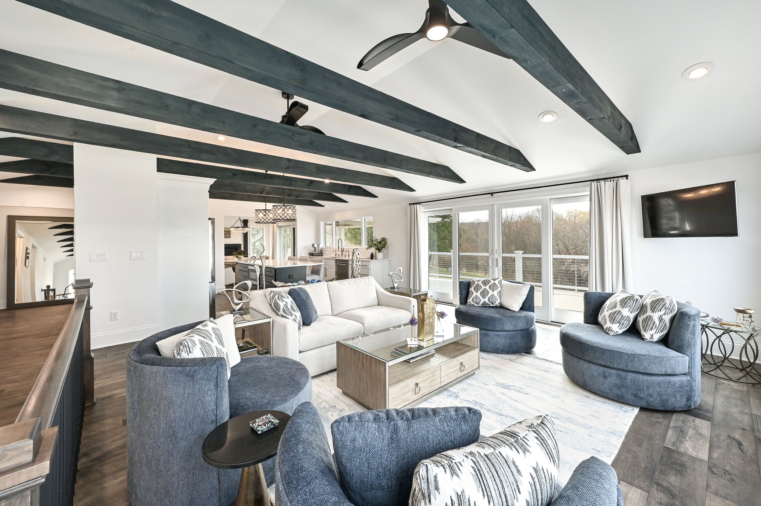 Living room with blue and white furniture, large windows, sliding glass doors, and black wooden ceiling beams.
