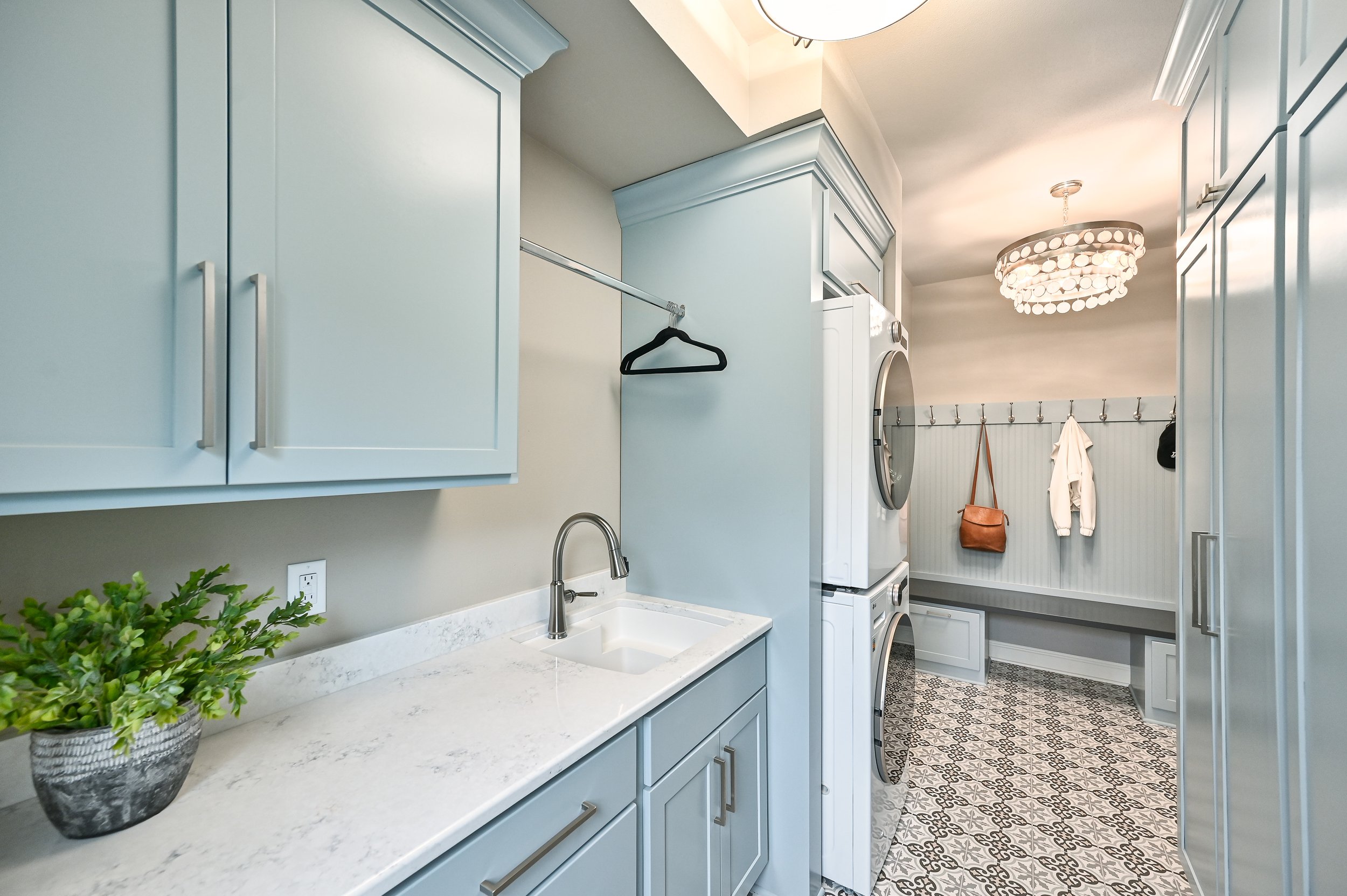 Laundry room with light blue cabinets, a white countertop, a small sink, laundry machines, and a coat rack with hanging items.