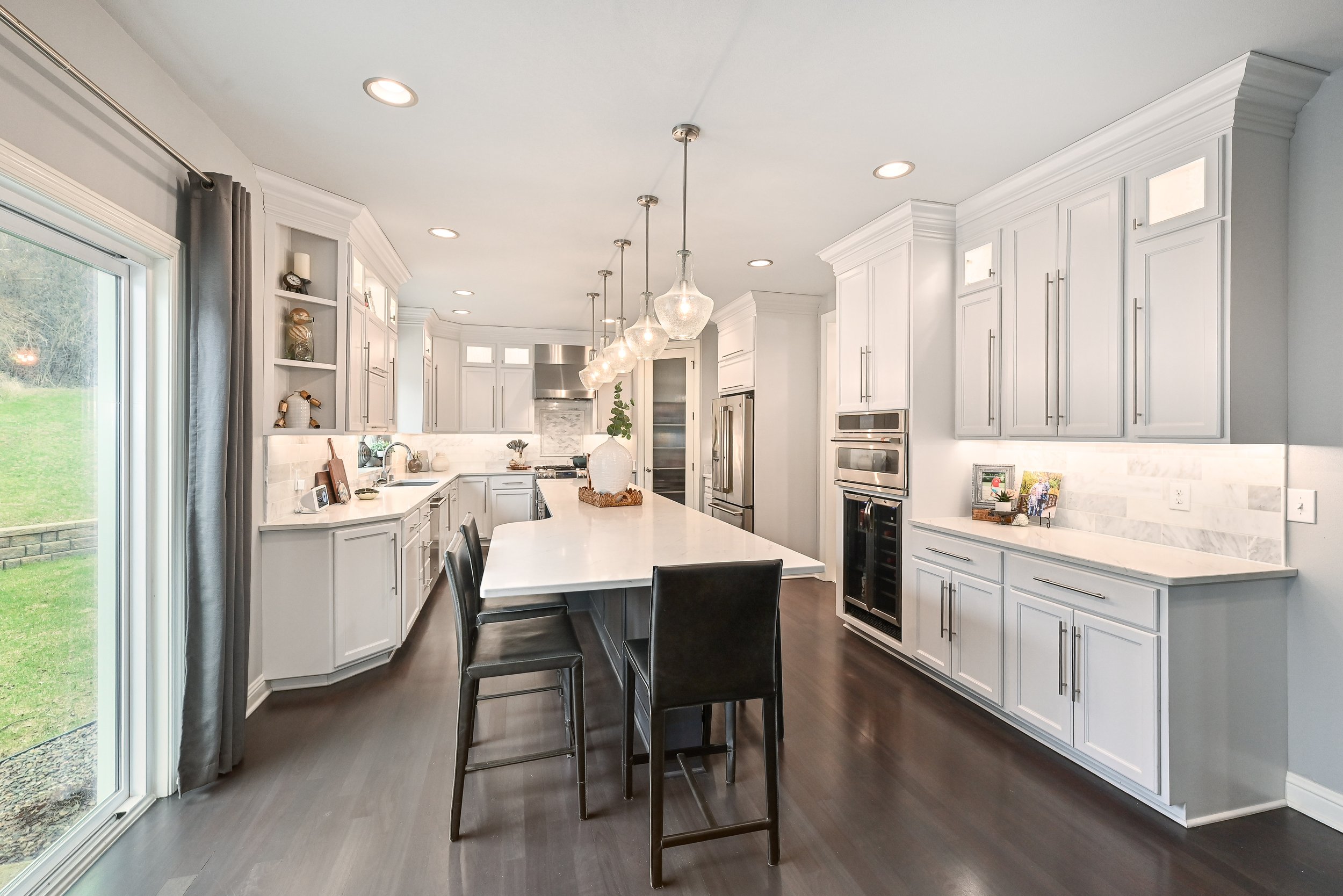 Modern kitchen with white cabinets, stainless steel appliances, dark wood flooring, and a large island with black barstools.