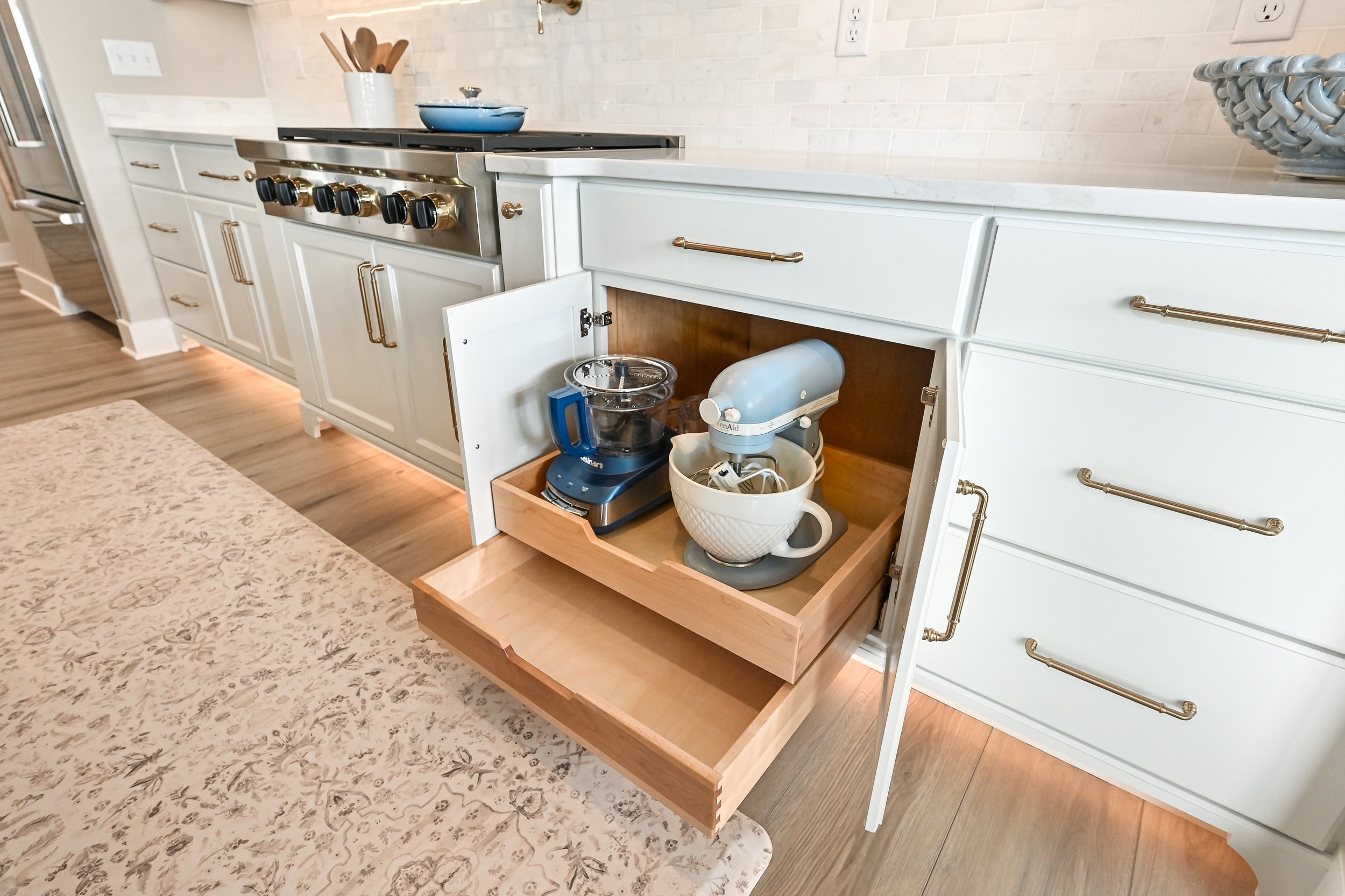 Open kitchen cabinet drawer with a stand mixer, a bowl, and a food processor inside.