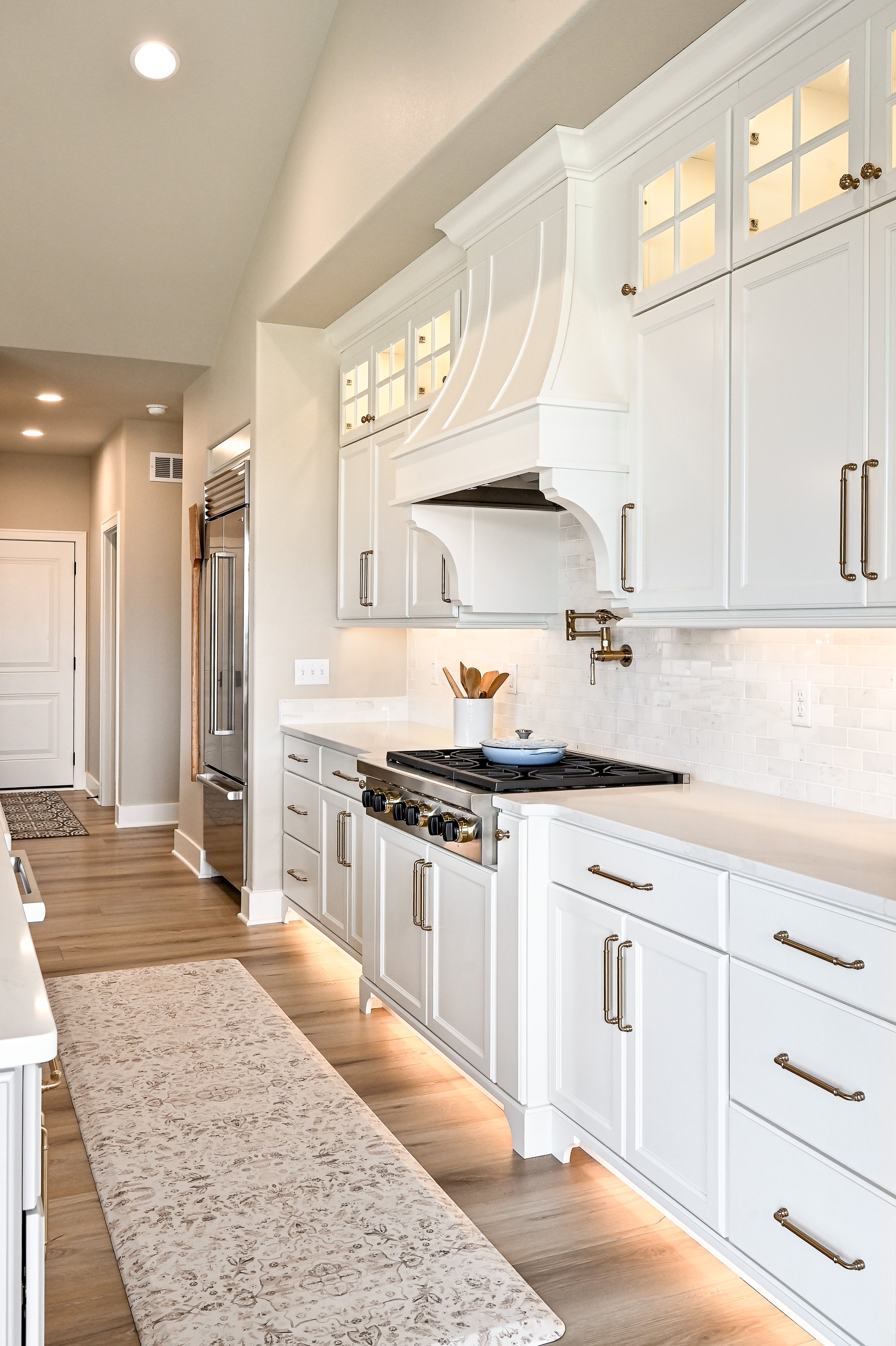 Modern white kitchen with cabinets, a stove, and a built-in range hood, illuminated with under-cabinet lighting and recessed ceiling lights.