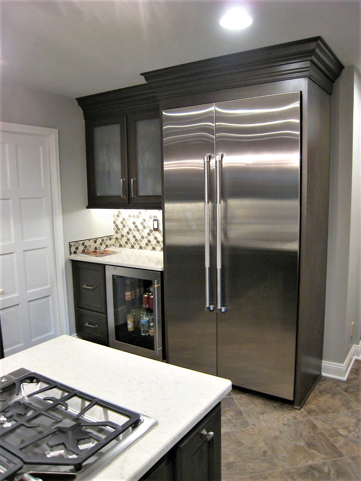 Kitchen with black cabinets, stainless steel refrigerator with double doors, small wine fridge, gas stove, and beige countertop.