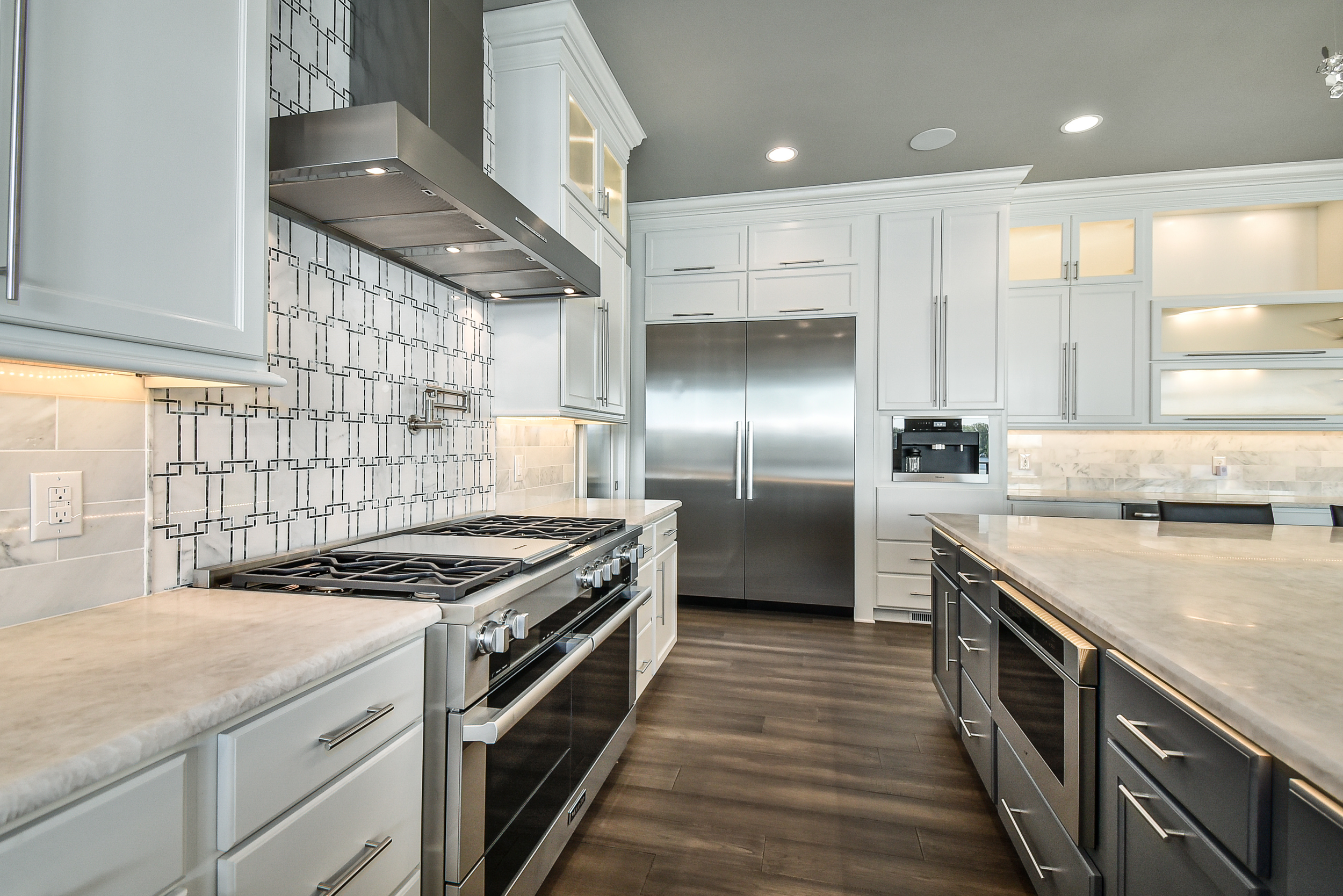 Modern kitchen with white cabinetry, stainless steel appliances, marble countertops, and a dark wood floor.