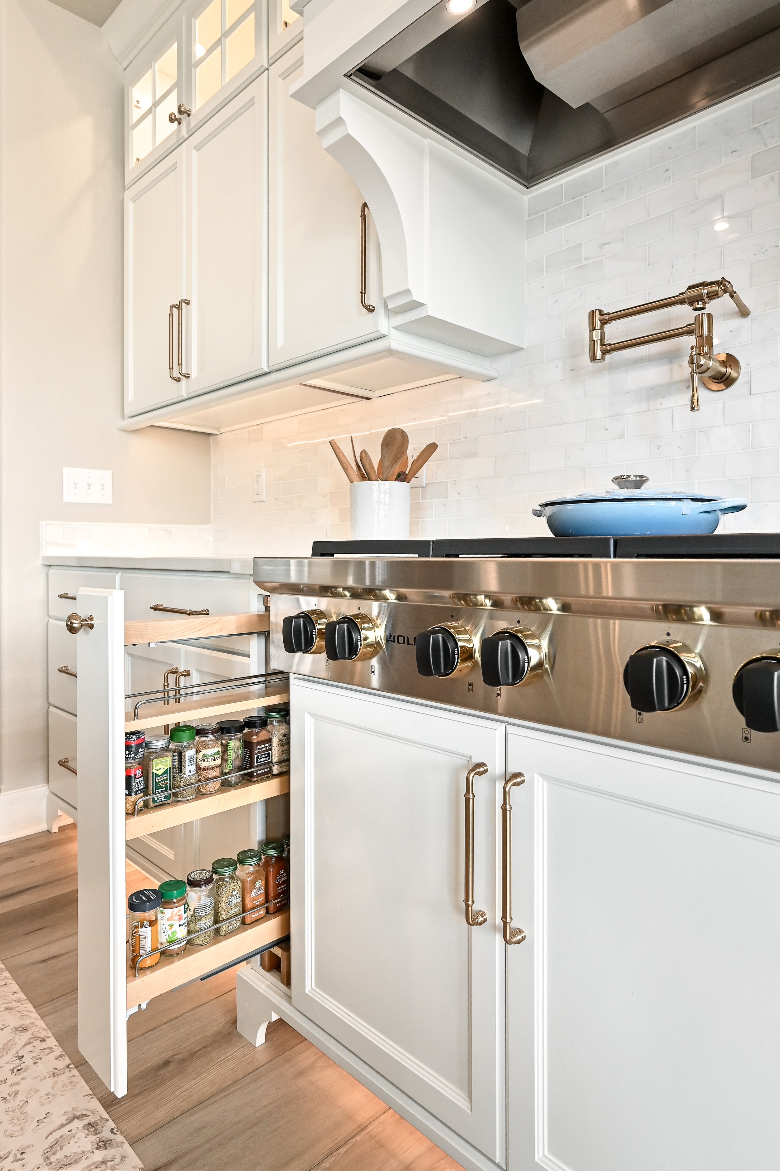 White kitchen with upper cabinets, a stove with gold knobs, a pull-out spice cabinet, and a white subway tile backsplash.