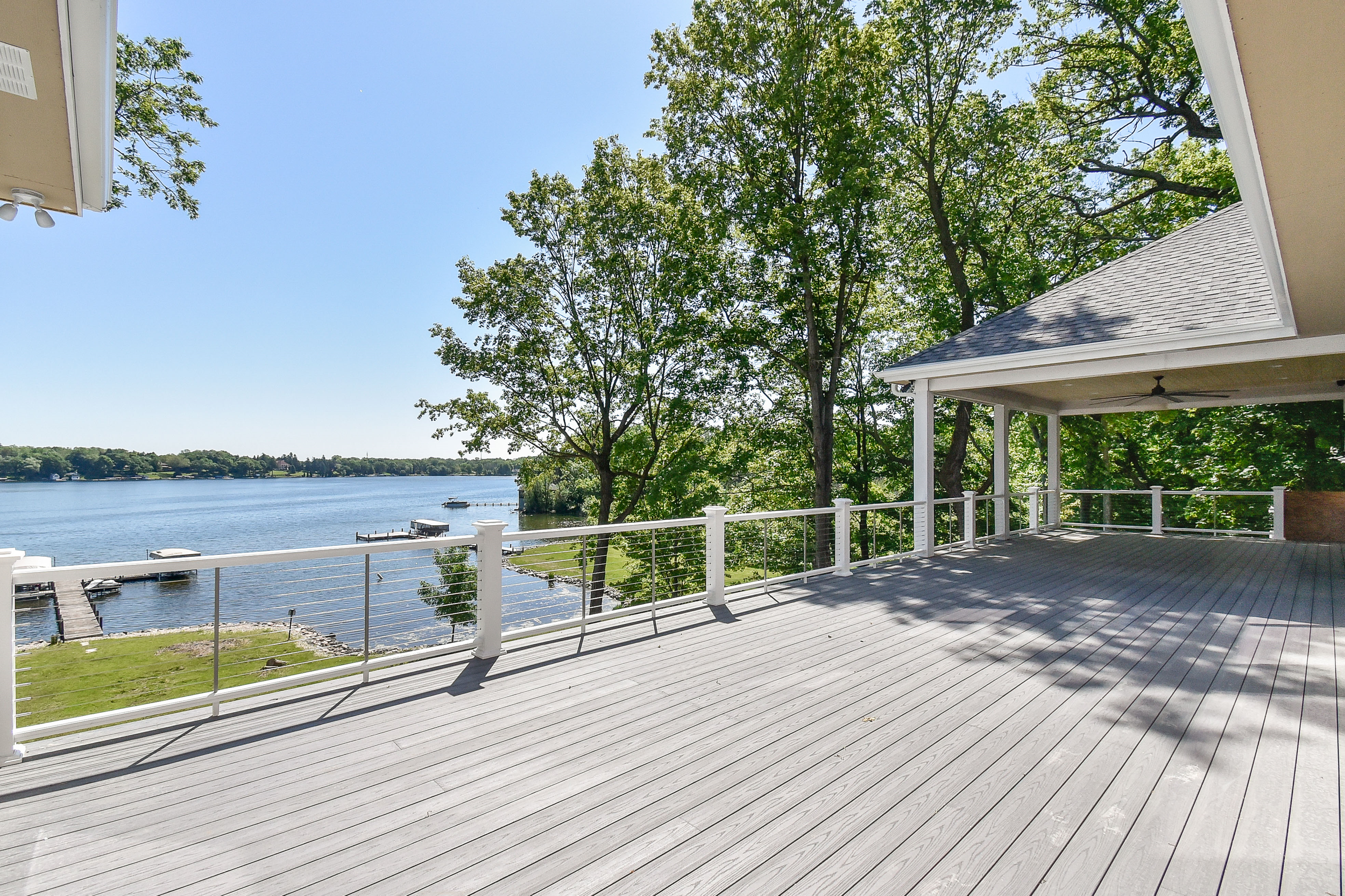 Spacious outdoor deck overlooking a lake with trees and boats in the water.