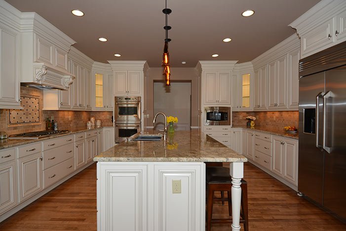 Large kitchen with white cabinets, granite island, stainless steel appliances, hardwood floors, and pendant lighting.