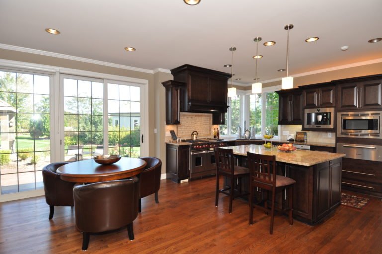 Open-concept kitchen and dining area with large sliding glass doors, dark wood cabinets, island with seating, and hardwood floors.