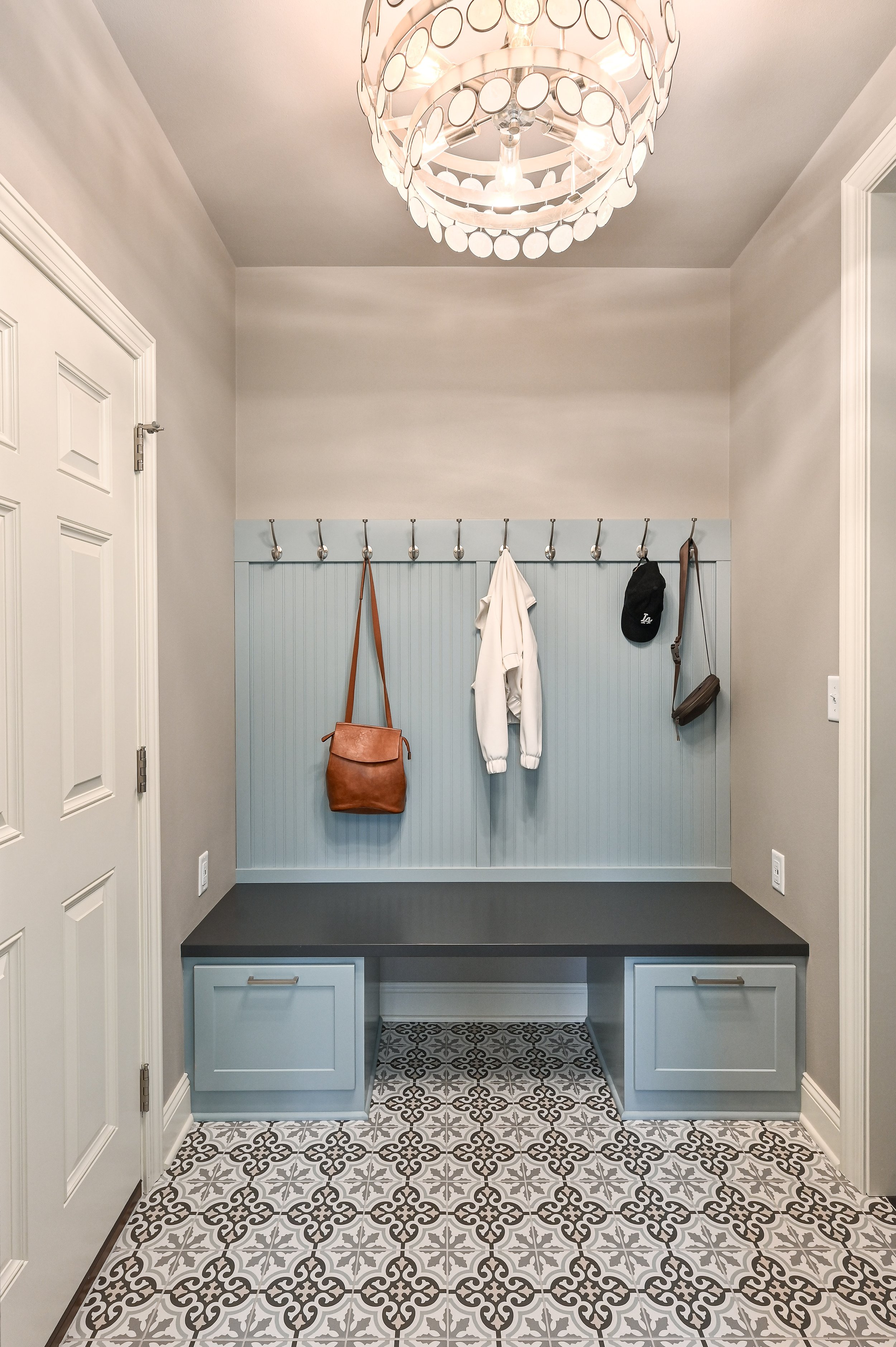 Entryway with a beadboard accent wall, hooks with hanging bags and clothes, a navy bench, and patterned tile floor tiles.