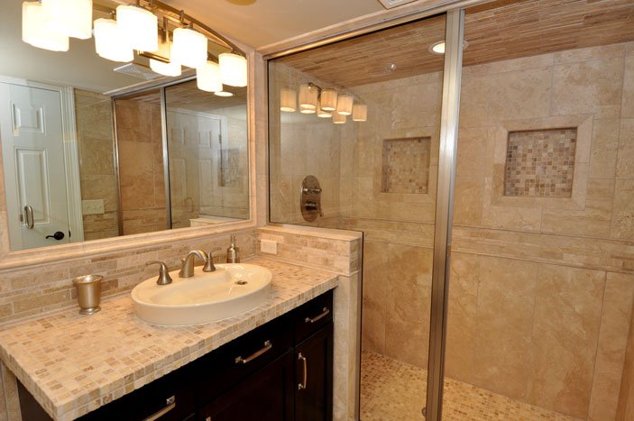 Bathroom sink with beige countertop and dark cabinetry, large mirror, and walk-in shower with tiled walls and glass door.