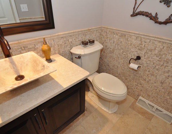Bathroom with marble sink, dark wood vanity, toilet, wall mirror, decorative mirror, soap dispenser, and toilet paper holder.