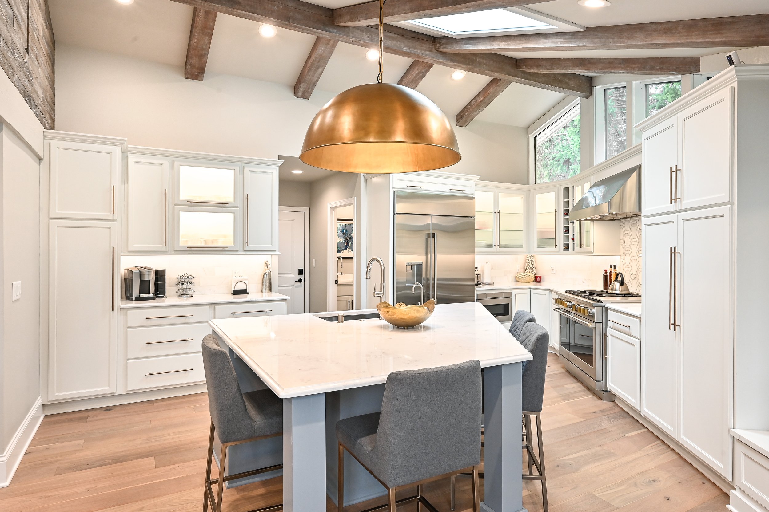 Modern kitchen with white cabinets, a large center island, pendant light, stainless steel appliances, and wood beams on the ceiling.
