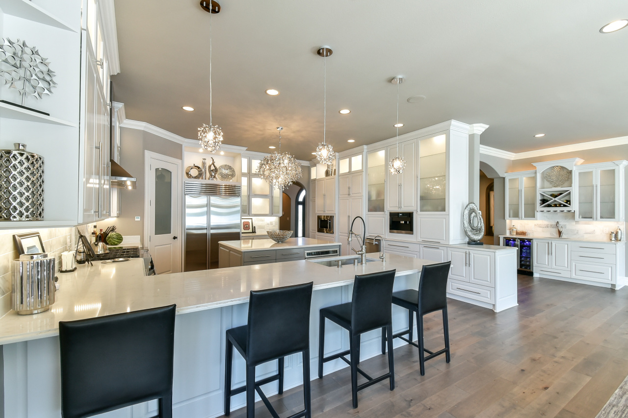 Modern kitchen with white cabinetry, a large central island, black barstools, stainless steel refrigerator, decorative pendant lights, and hardwood floors.