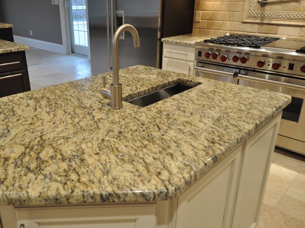 Kitchen island with granite countertop, built-in sink, and modern faucet in a spacious kitchen with a stainless steel stove in the background.