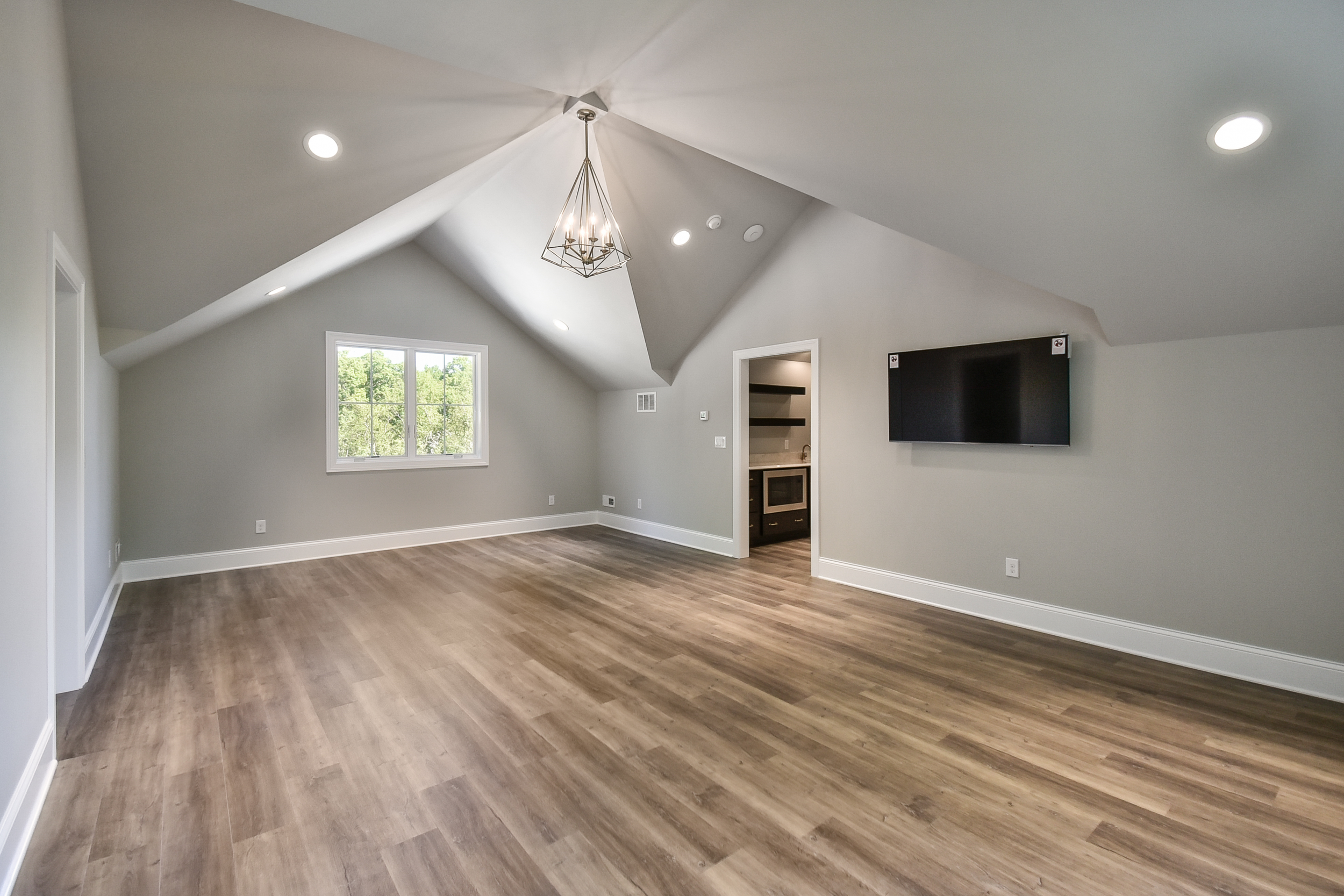 Empty living room with wood floors, white walls, a window, a mounted flat-screen TV, and a small open area with a fireplace.