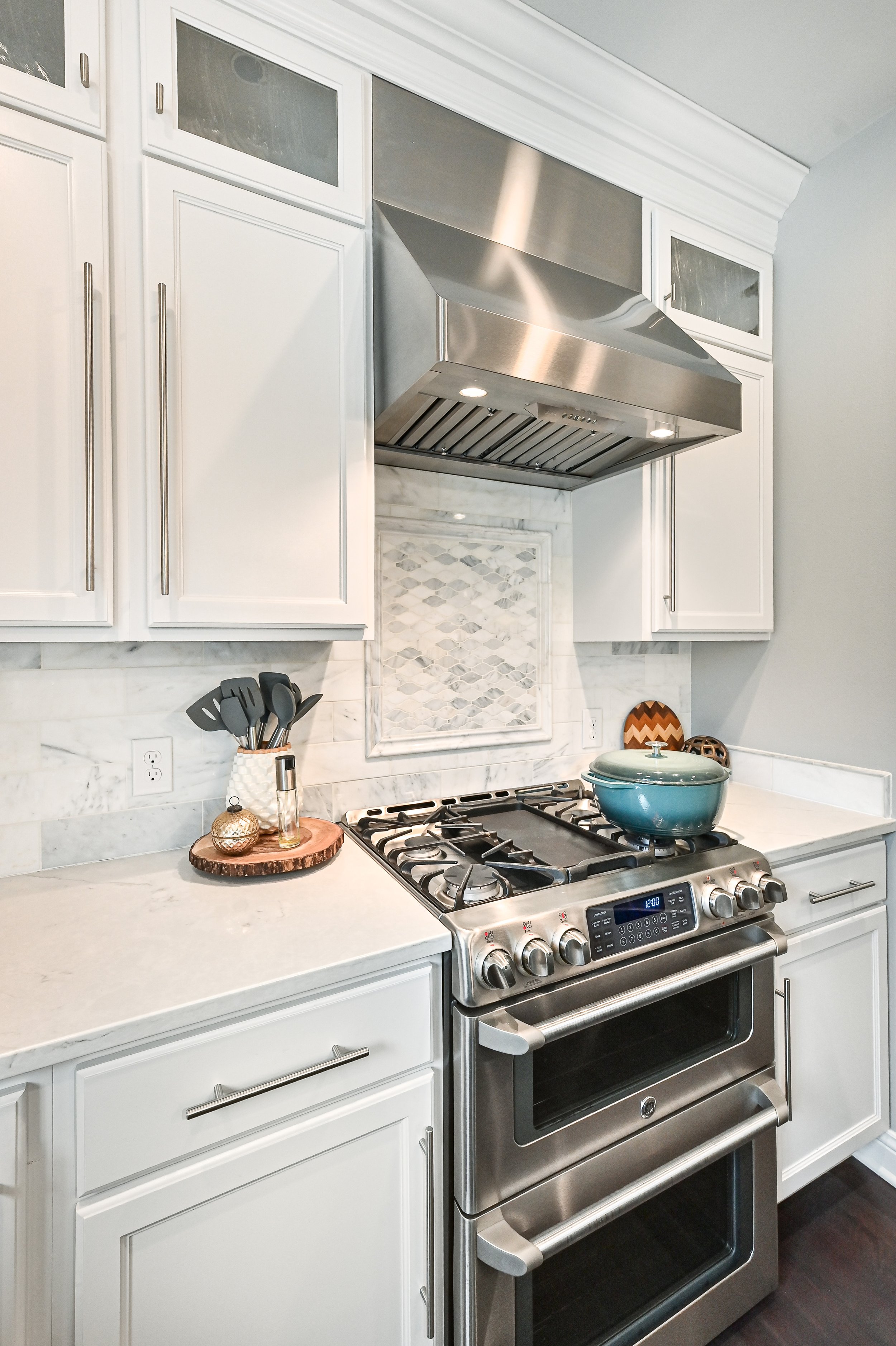 Modern kitchen with white cabinets, marble backsplash, stainless steel oven and range hood, and decorative items on the countertop.