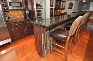 Kitchen island with a stone countertop and wooden base, with four barstools lined up along one side. The background shows kitchen cabinets, a microwave, and decorative wall art.