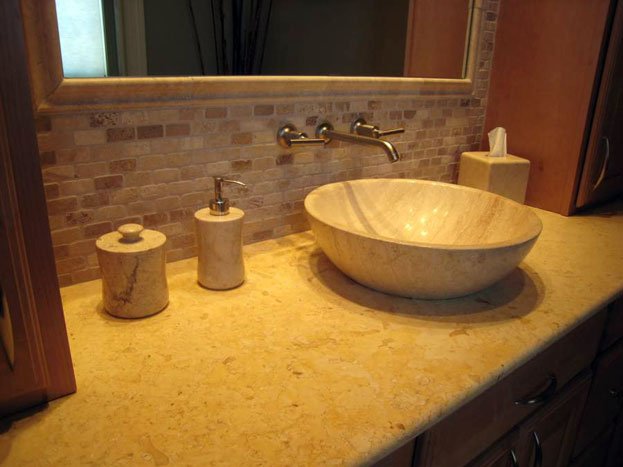Bathroom vanity with a stone vessel sink, soap dispenser, toothbrush holder, mirror, and tissue box.