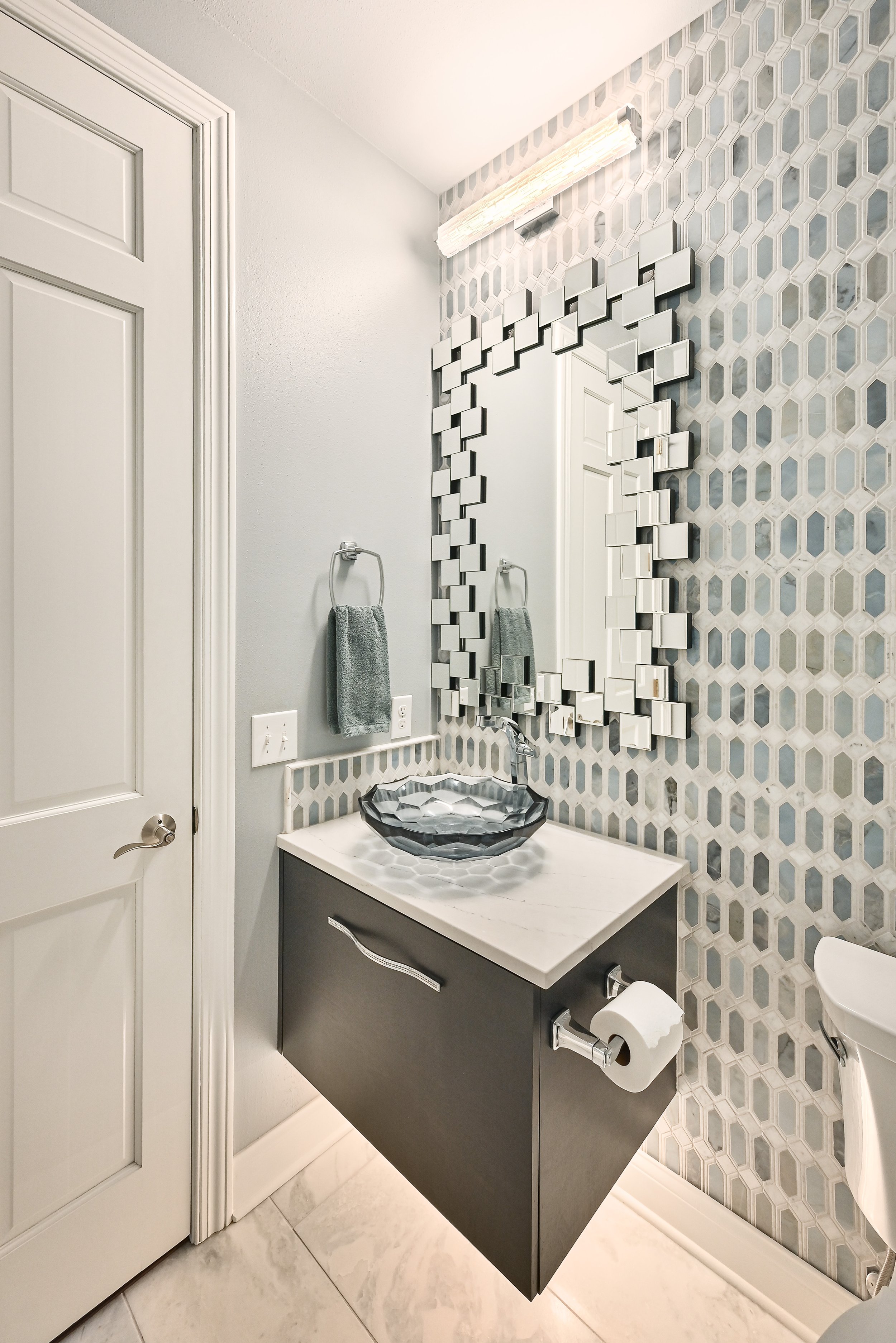 Modern bathroom with a decorative mirror, geometric vessel sink, and patterned tile wall.