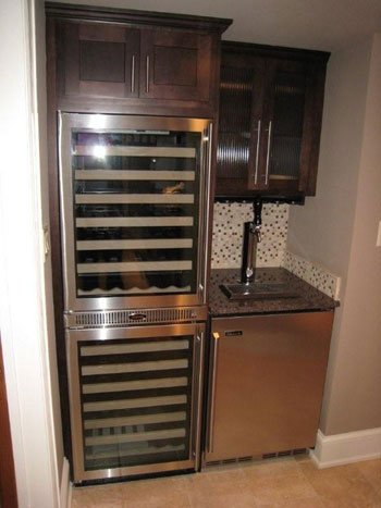 A small wet bar or kitchenette with a built-in wine cooler and a mini refrigerator, dark wood cabinets, a small sink, and a tile backsplash.