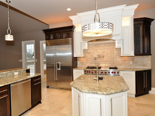 Kitchen with granite countertops, a central island, a stainless steel refrigerator, modern pendant lighting, and a range hood above a stove with red knobs, white and dark wood cabinetry, and a tiled backsplash.