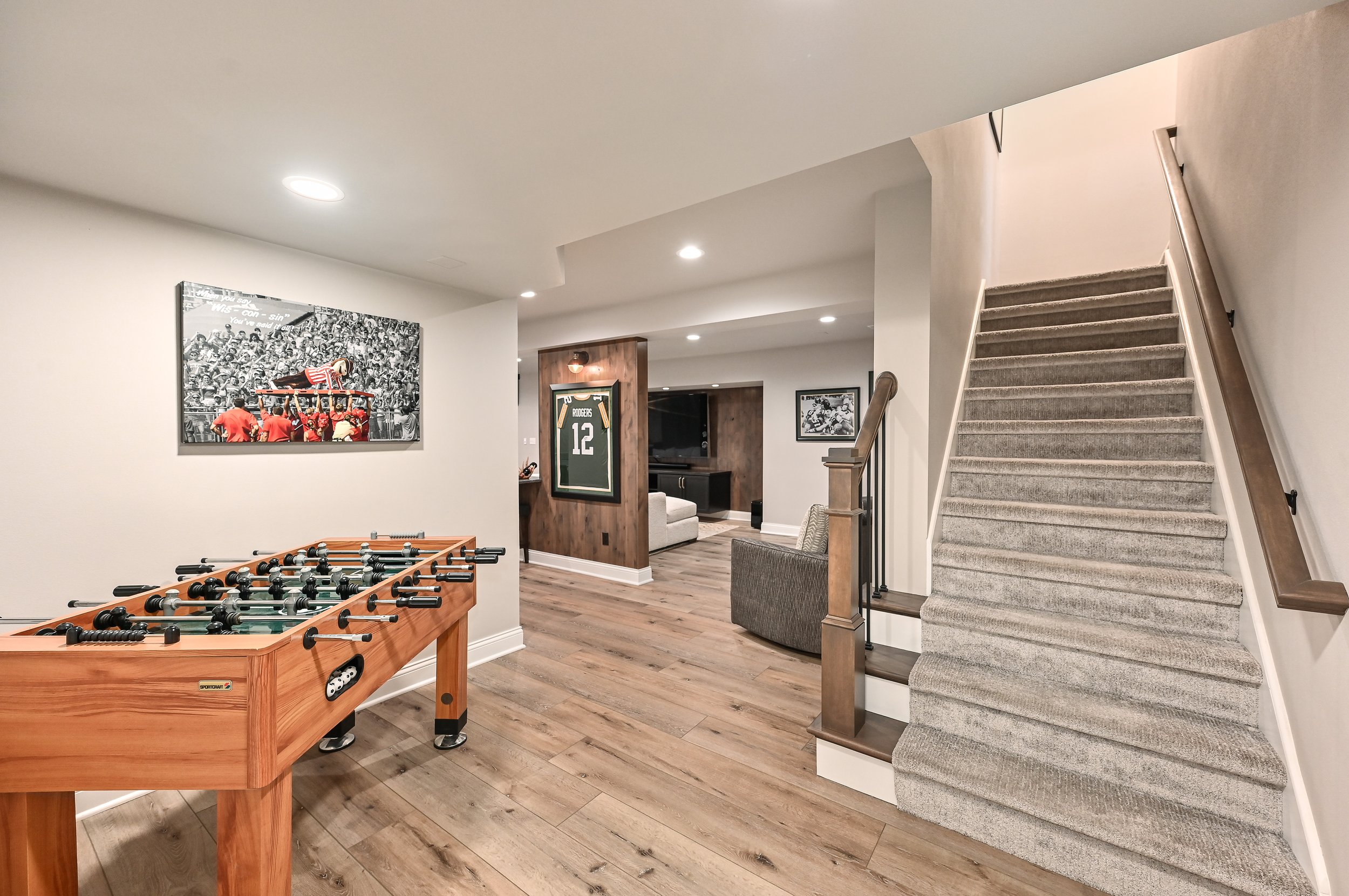 view of a basement with a foosball table, sports posters, a staircase, a TV area, and sports memorabilia.