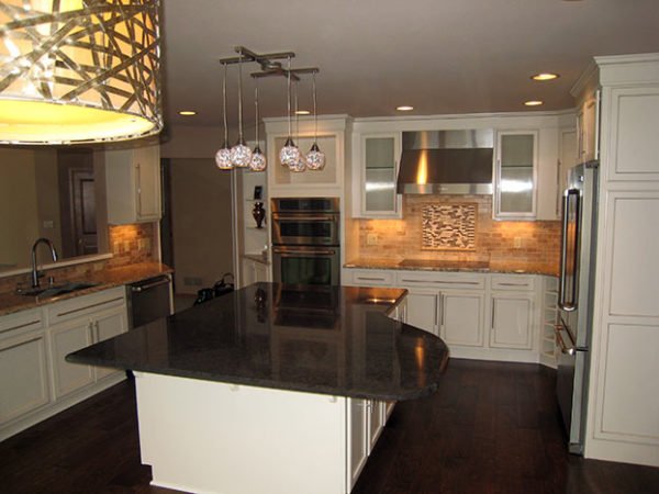 Modern kitchen with white cabinets, a large dark island, backsplash tiles, pendant lighting, stainless steel appliances, and hardwood floors.