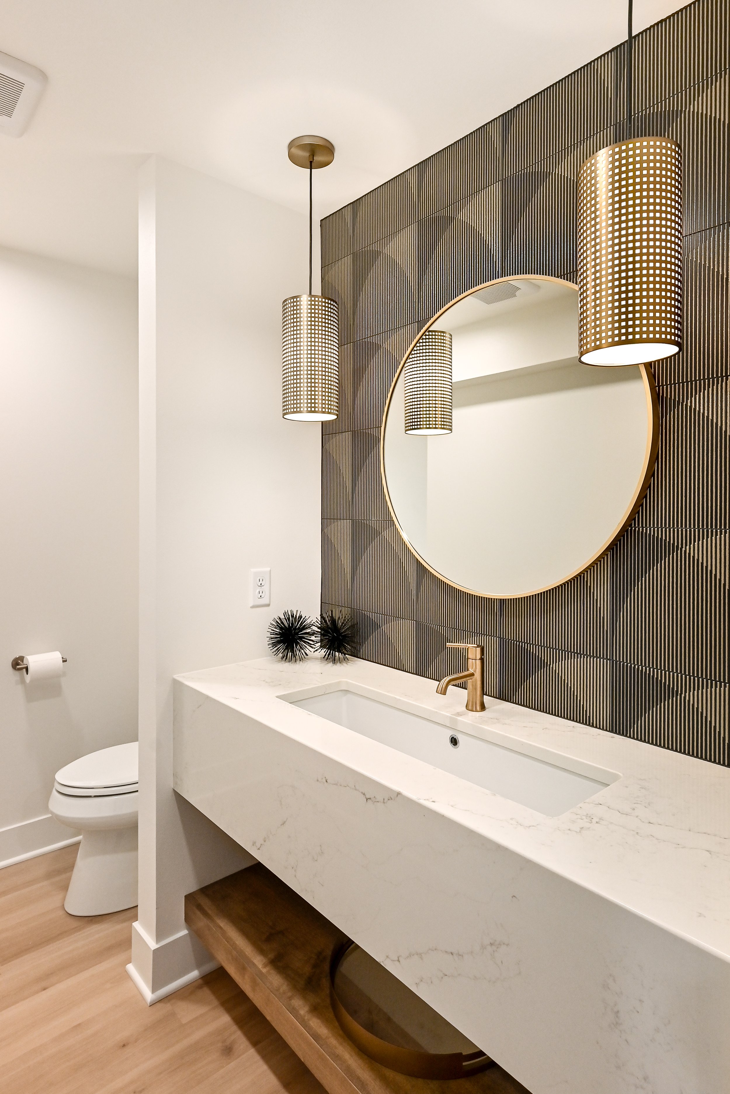 Modern bathroom with a white marble vanity, round mirror, black decorative accents, pendant lighting, and a toilet.