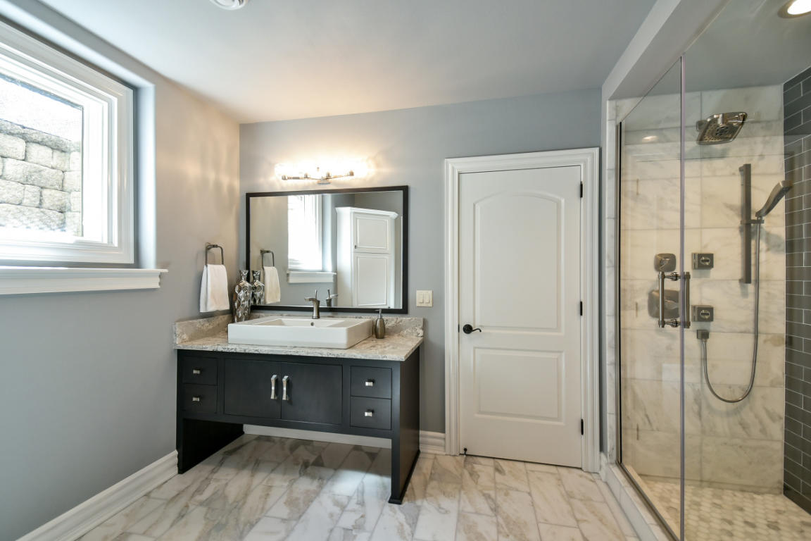 Modern bathroom with a black vanity, a large mirror, a vessel sink, towel rack, window, and a glass-enclosed shower with marble tiles.