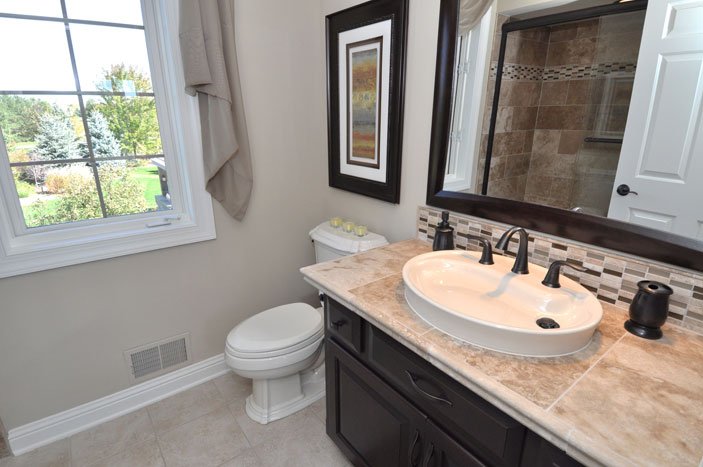 Bathroom with a window, toilet, vanity with a sink, mirror, and shower area in the background.