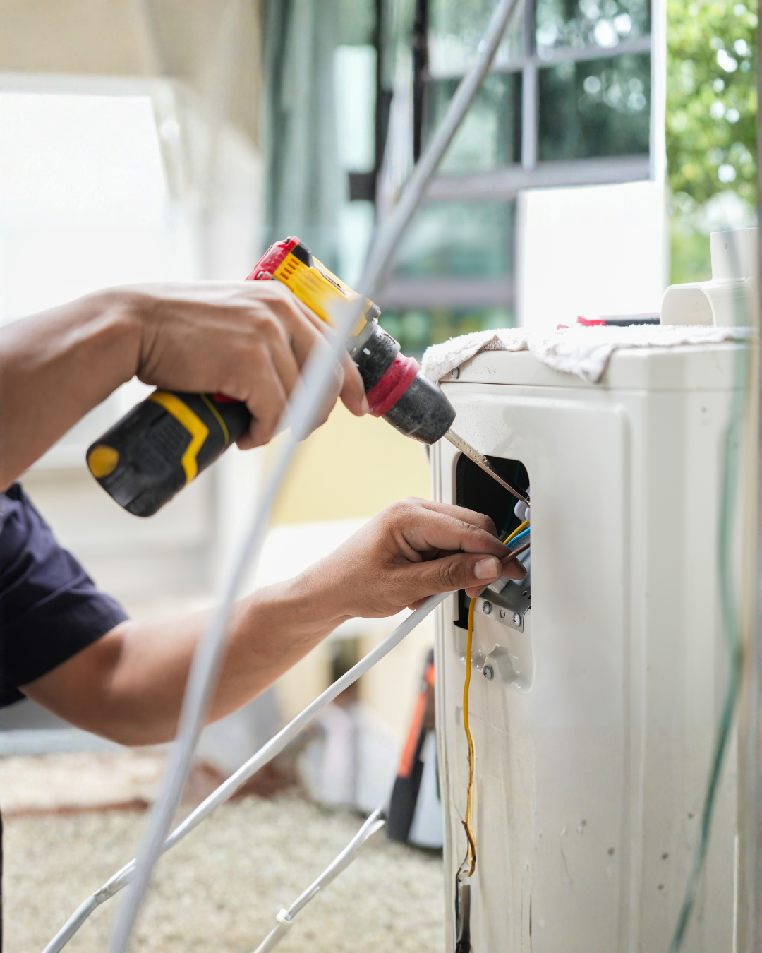 A person repairing an electrical appliance using a cordless drill and working on wires inside the appliance.