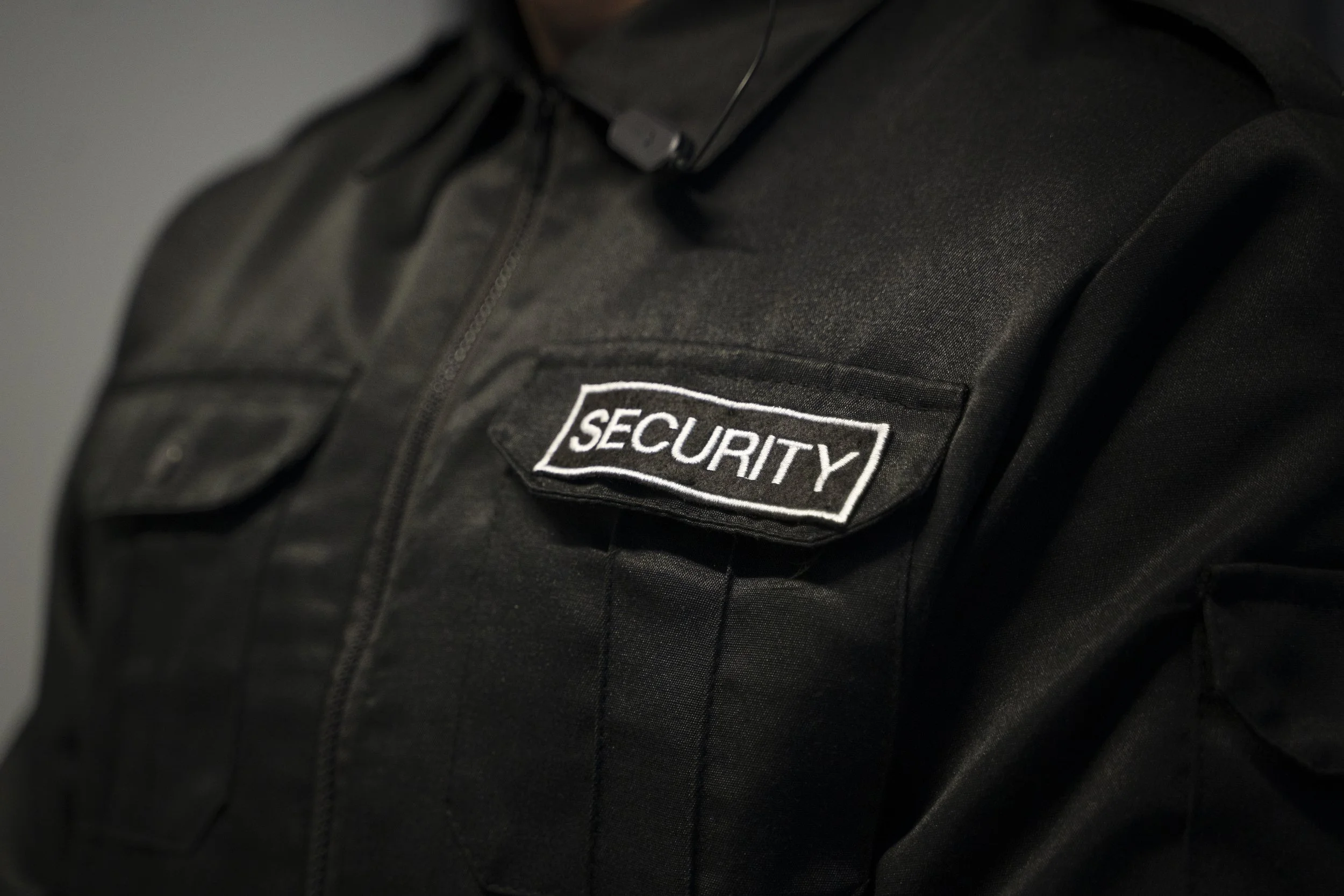 Close-up of a black security guard uniform with a patch that says 'SECURITY' on the chest.
