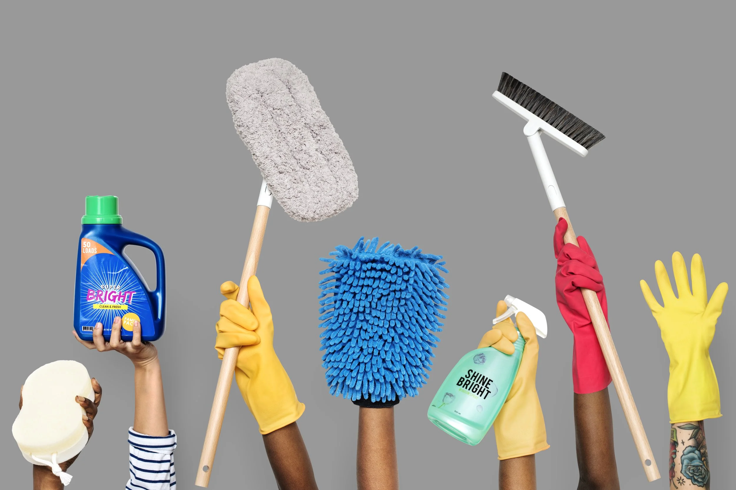 Six hands wearing yellow and red gloves holding various cleaning tools and supplies against a gray background, including a bottle of bright cleaning liquid, a white sponge, a gray duster, a blue microfiber cloth, a spray bottle, and another cleaning tool.