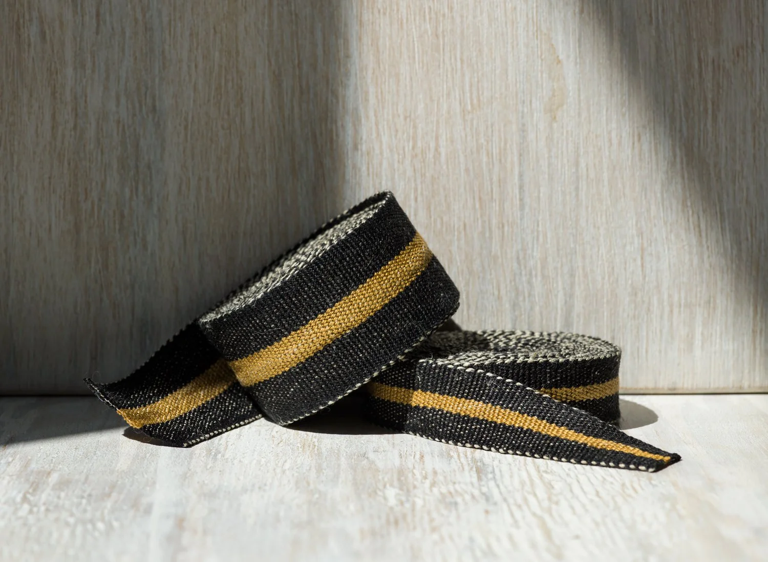 Stack of Modern Neutral I: Black and Bronze handwoven linen tape trim in black with a bold bronze band in narrow and medium widths.