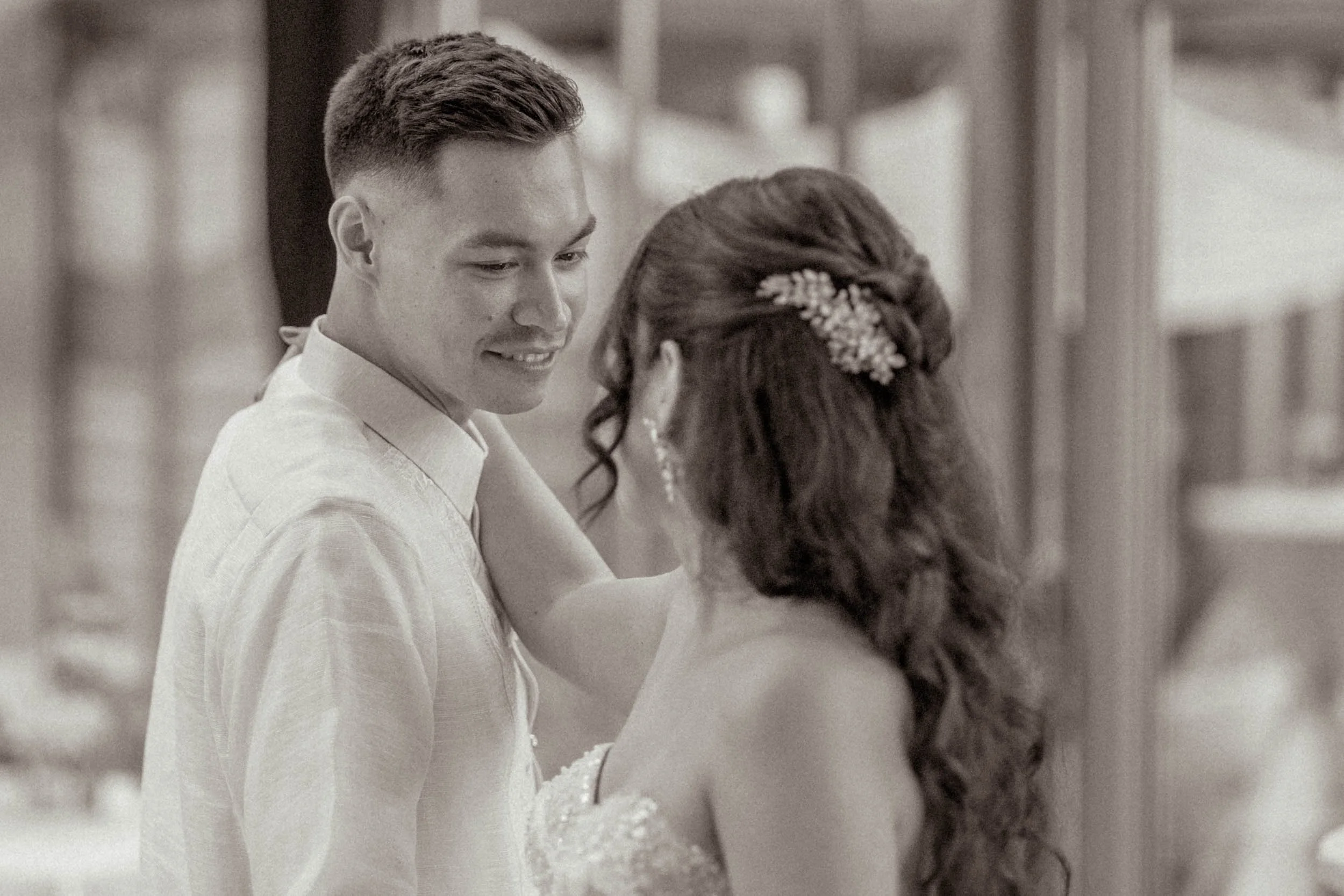 Ein junges Paar bei einer Hochzeit, sie tanzen eng umschlungen, die Frau trägt ein Hochzeitskleid mit lockigem Haar und Haaraccessoire, der Mann trägt ein Hemd, beide sehen glücklich aus.