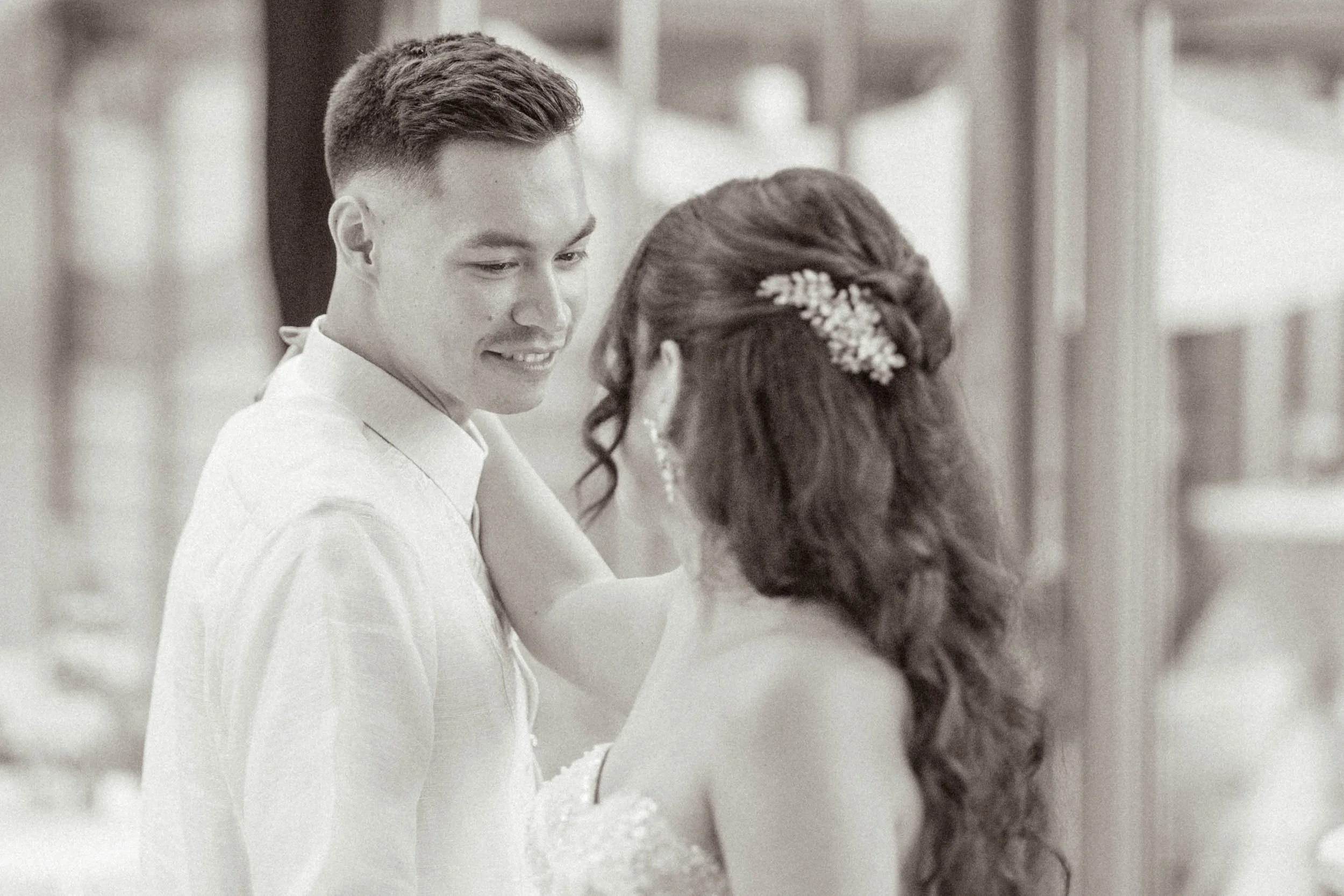 Ein junges Paar bei einer Hochzeit, der Mann trägt einen weißen Hemd, die Frau hat lockiges Haar mit einer Haarklammer und trägt ein Hochzeitskleid.