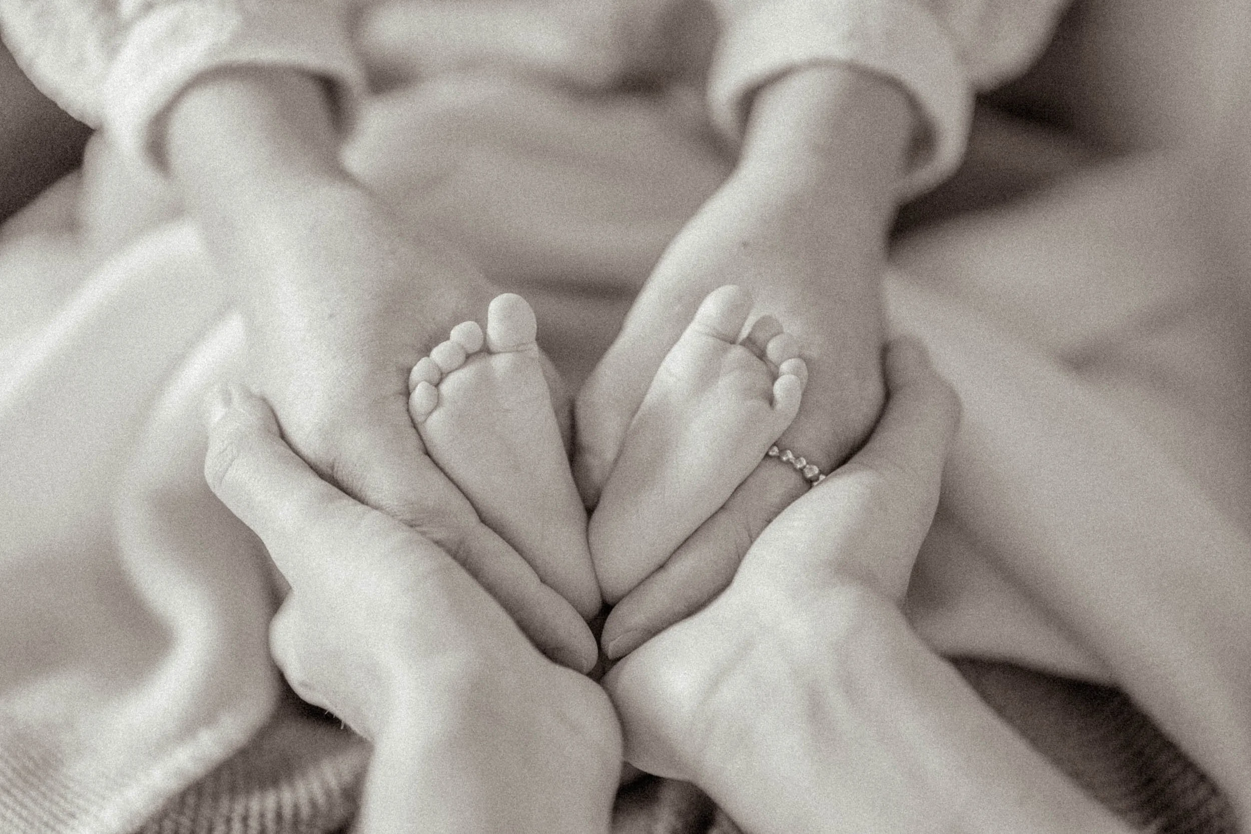 Nahaufnahme von Händen von Erwachsenen, die winzige Babyfüße wie ein Herz halten.