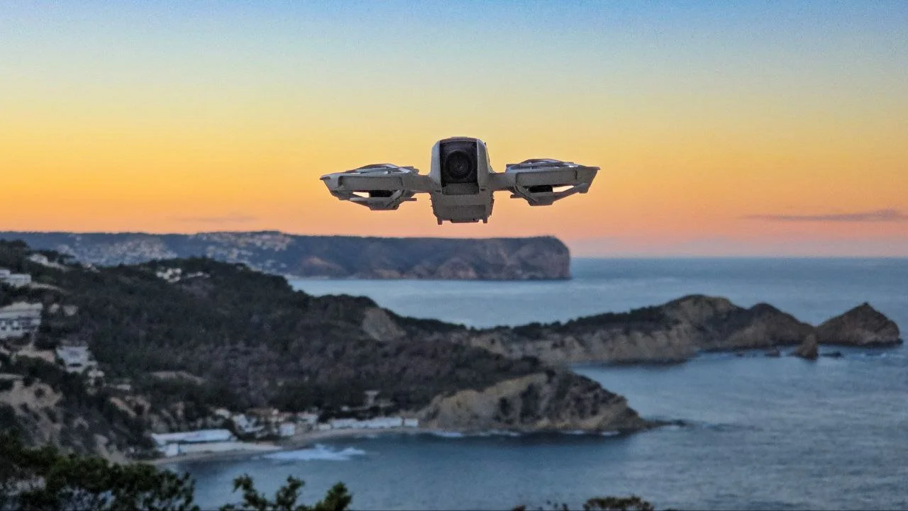 A drone flying over a coastal landscape at sunset with cliffs and ocean in the background.