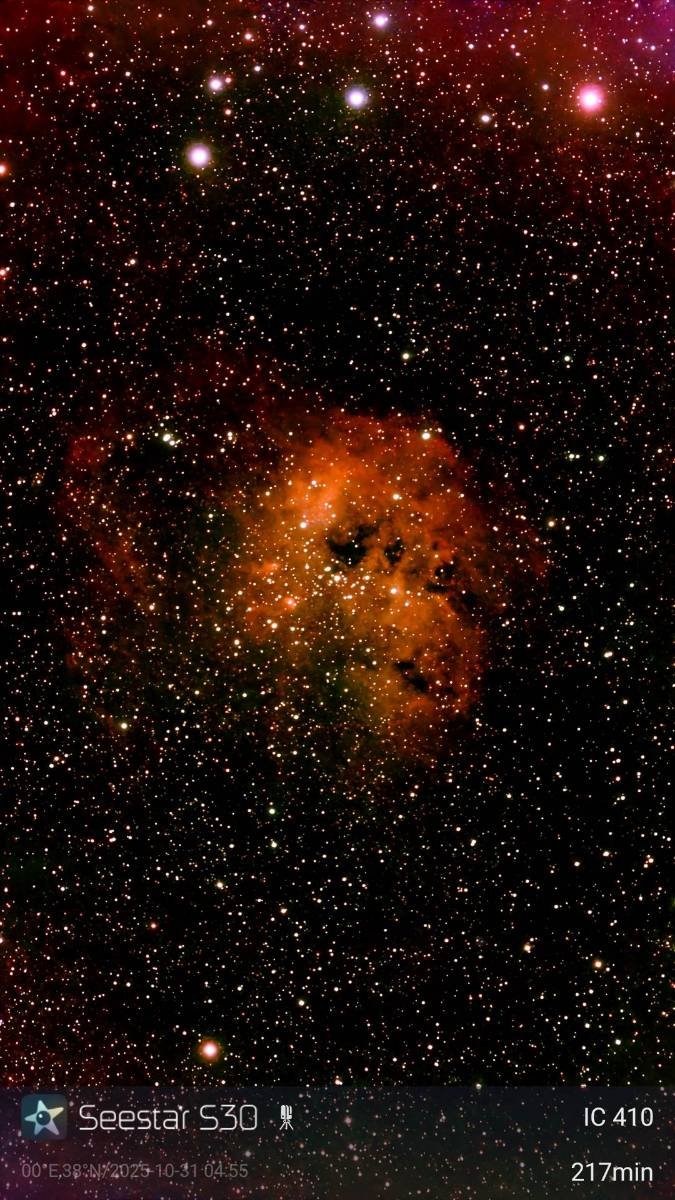 Deep space image showing numerous stars and a glowing nebula in the center with reddish and orange colors.