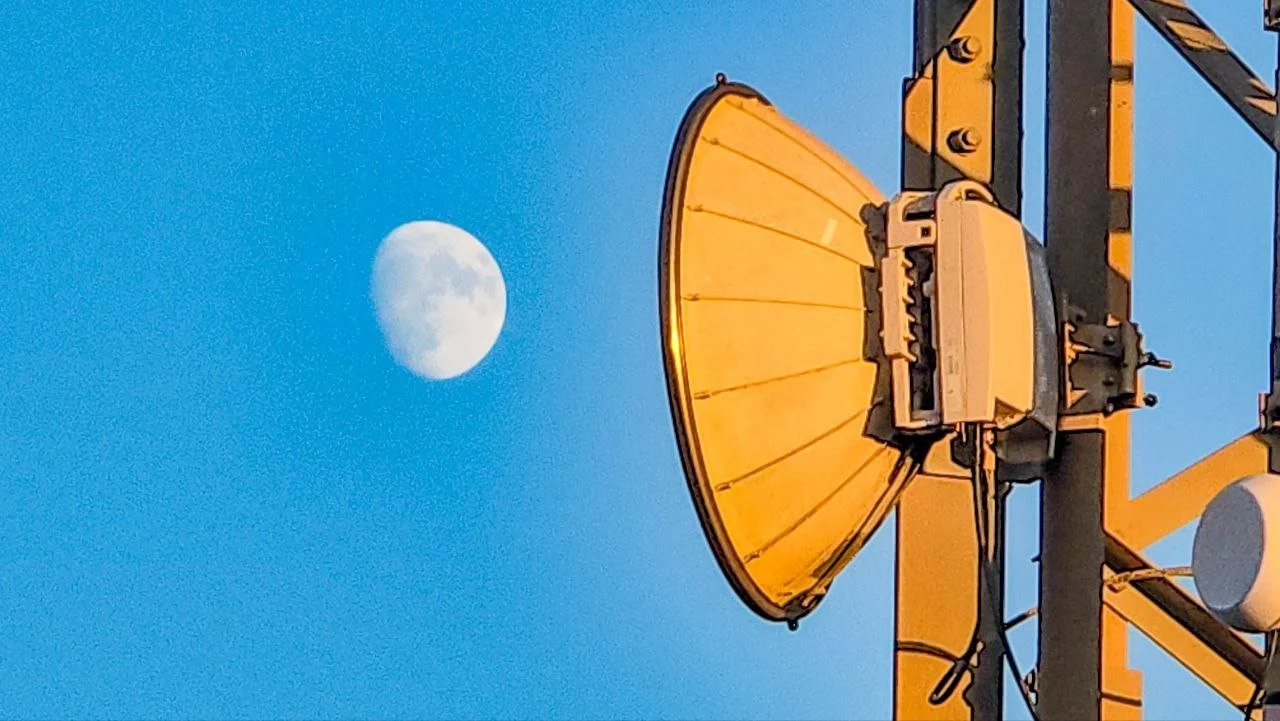A satellite dish antenna pointing towards the sky with the moon visible in the background.